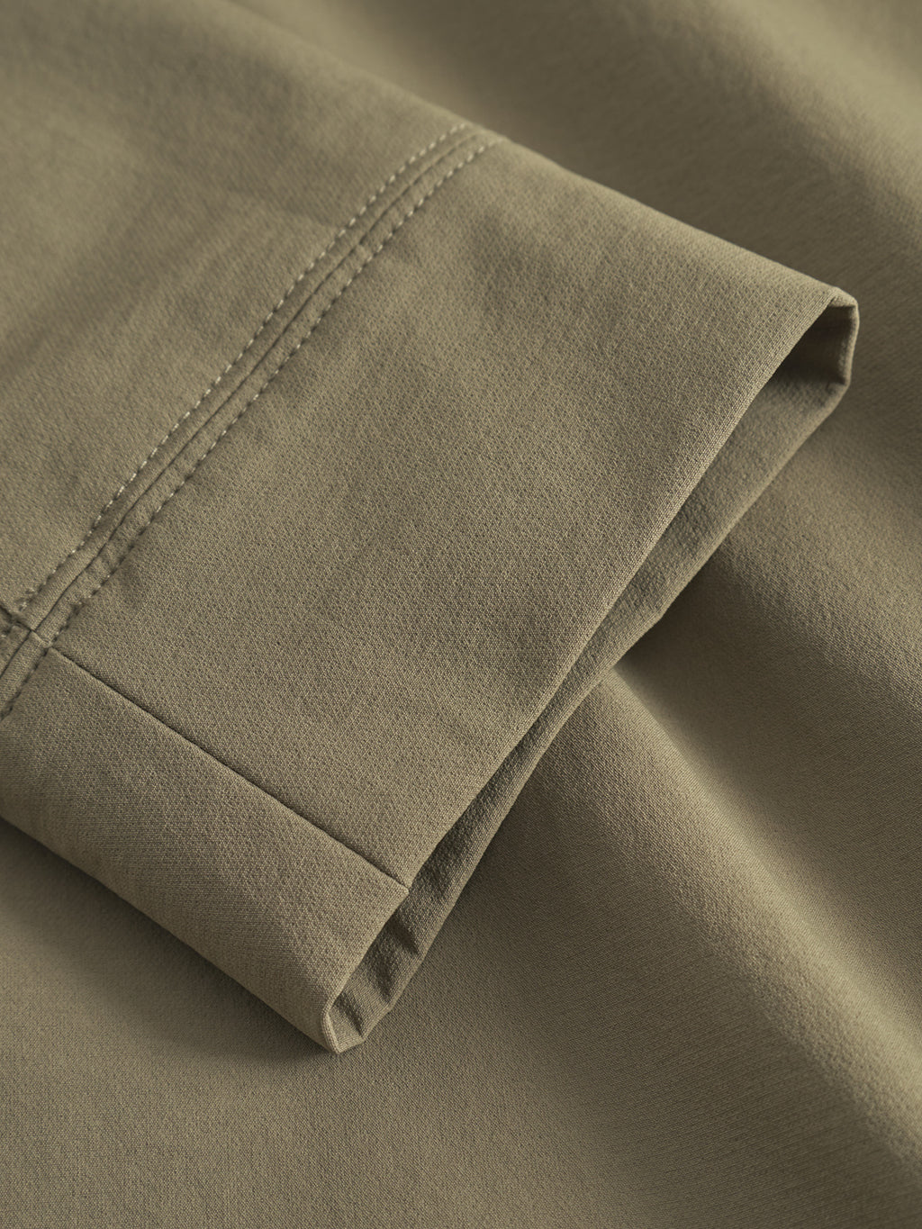 Close-up of a hemmed edge on the Gabba GABnik Tech - Army jacket, featuring double stitching and smooth olive-green fabric—details that highlight the quality and modern design of this practical tech jacket.