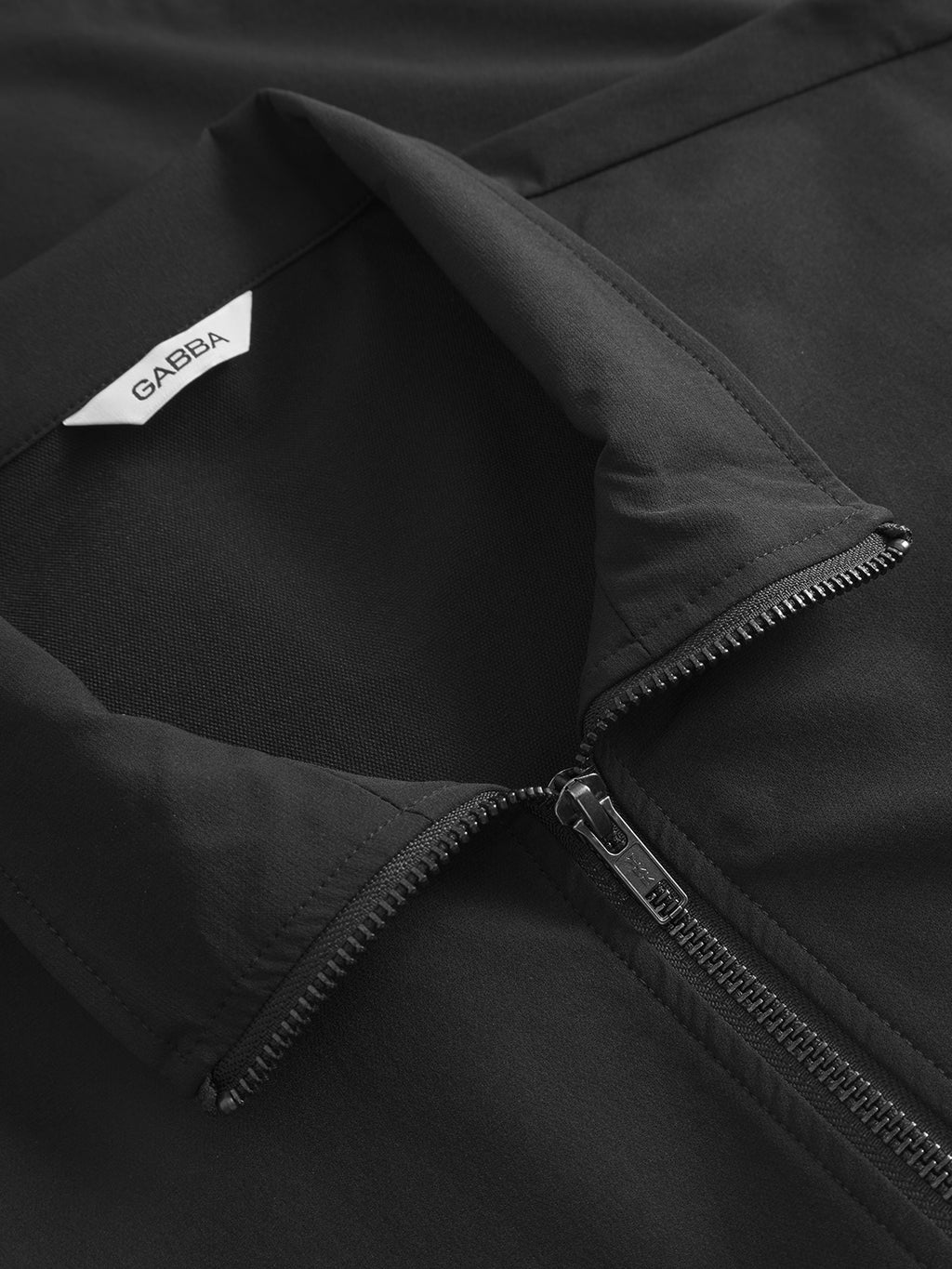 Close-up of the black GABnik Tech jacket by Gabba, featuring a zipper and folded collar. A white inner tag displays 