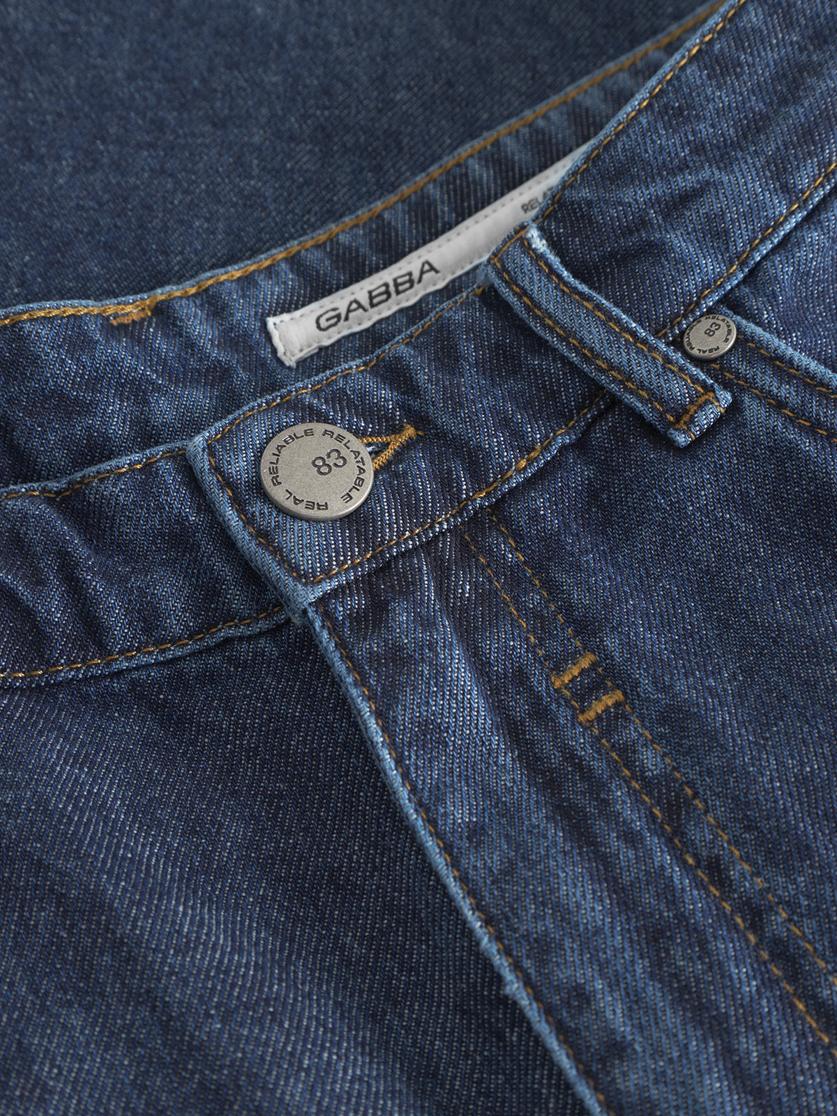 Close-up of Gabbas Ugo Cargo Fone in mid-blue denim. These loose-fitting shorts feature a metal button, yellow stitching, and a faded texture. A visible size 32 tag is located behind the button, enhancing the workwear vibe with its signature GABBA label.