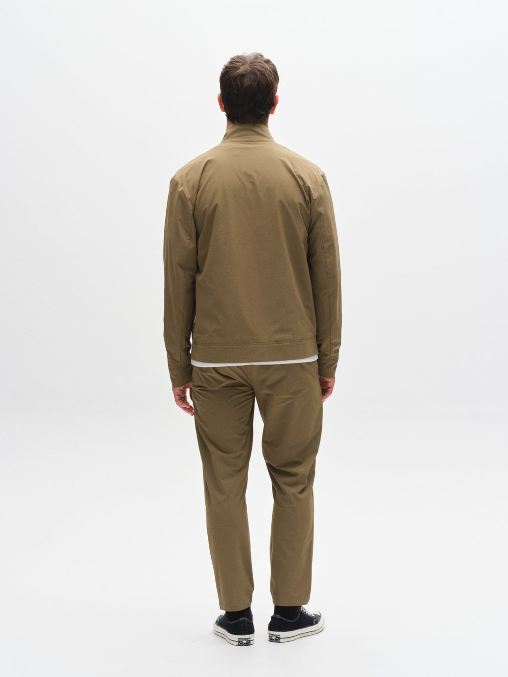 A man stands facing away from the camera, wearing Gabba GABmonza Tech - Army pants and a light brown jacket with black shoes, set against a plain white background.