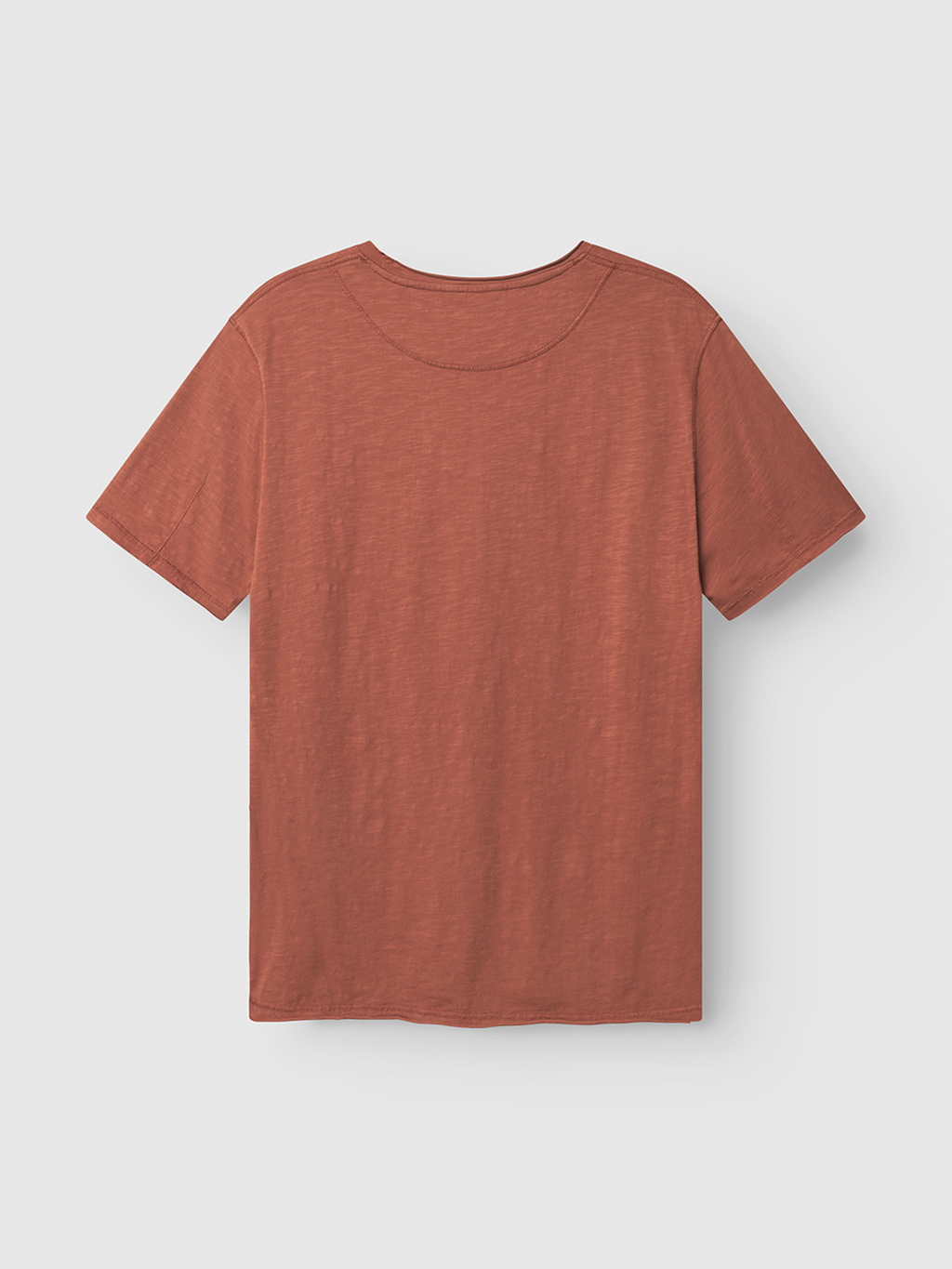 The Gabba Kostant New SS in Brown Rust is shown laid flat on a light gray background, highlighting the back of this relaxed-fit cotton short-sleeve t-shirt.
