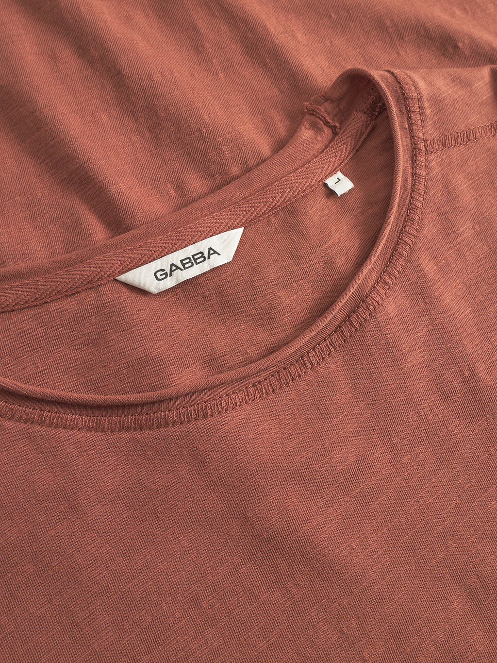 Close-up of the Gabba Kostant New SS t-shirt in brown rust, laid flat to highlight the neckline, fine stitching, and inner brand label—a vintage-inspired piece made from breathable cotton.