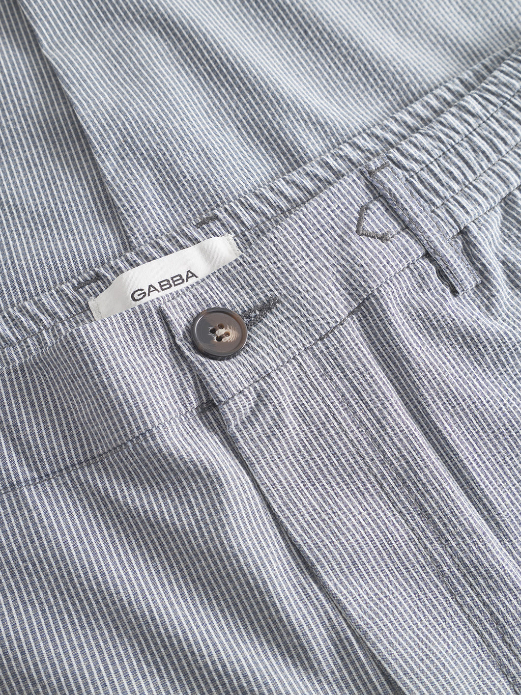 Close-up of Monza Button Com2 - Navy pants by Gabba, featuring a brown button, elastic waistband, and a visible white fabric label.