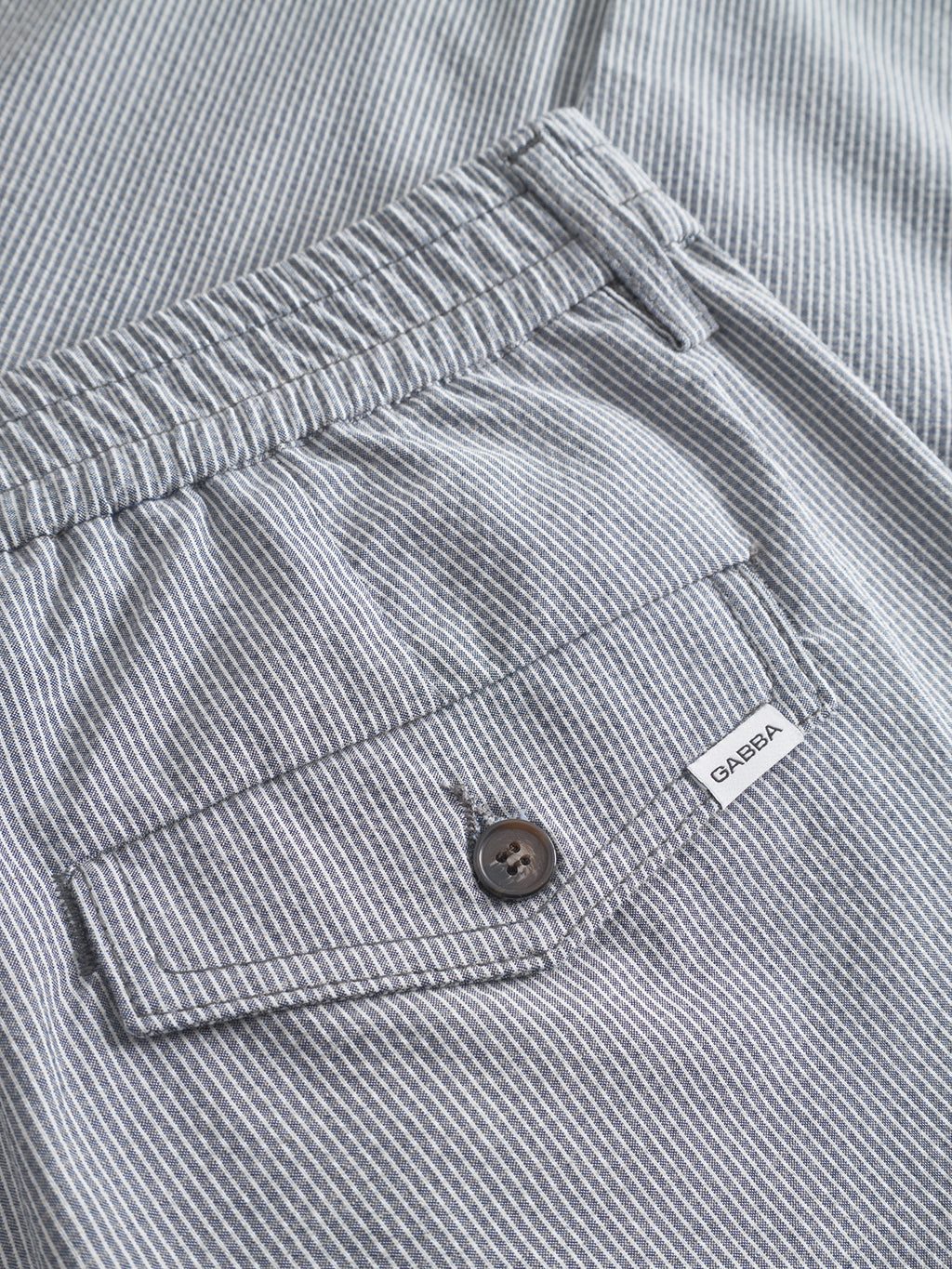Close-up of Monza Button Com2 - Navy pants by Gabba, featuring a navy pinstriped design, elastic waistband, buttoned back pocket, and a small white Gabba tag.