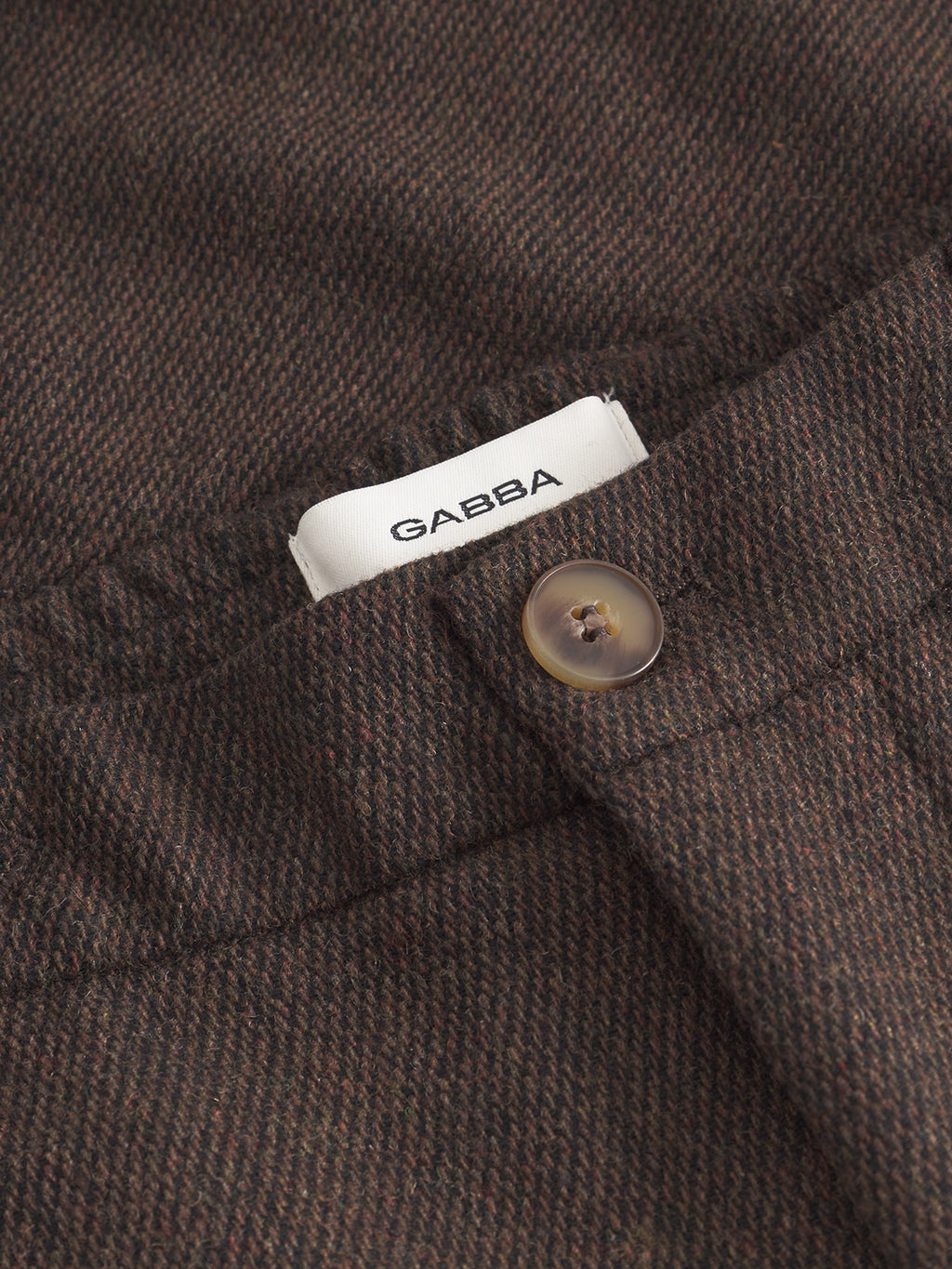 Close-up of Gabba Monza Wook - Brown textured fabric pants featuring a button and a partially visible white waistband label.