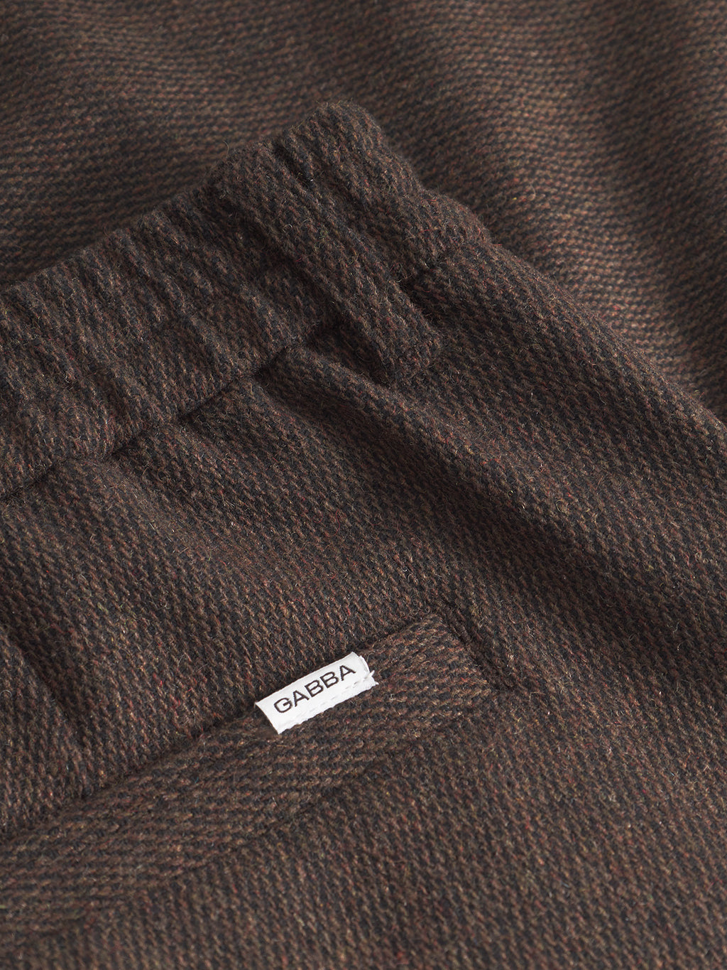 Close-up of the Monza Wook - Brown by Gabba, showing its textured dark brown fabric, elastic waistband, and a small white Gabba label stitched near the pocket.