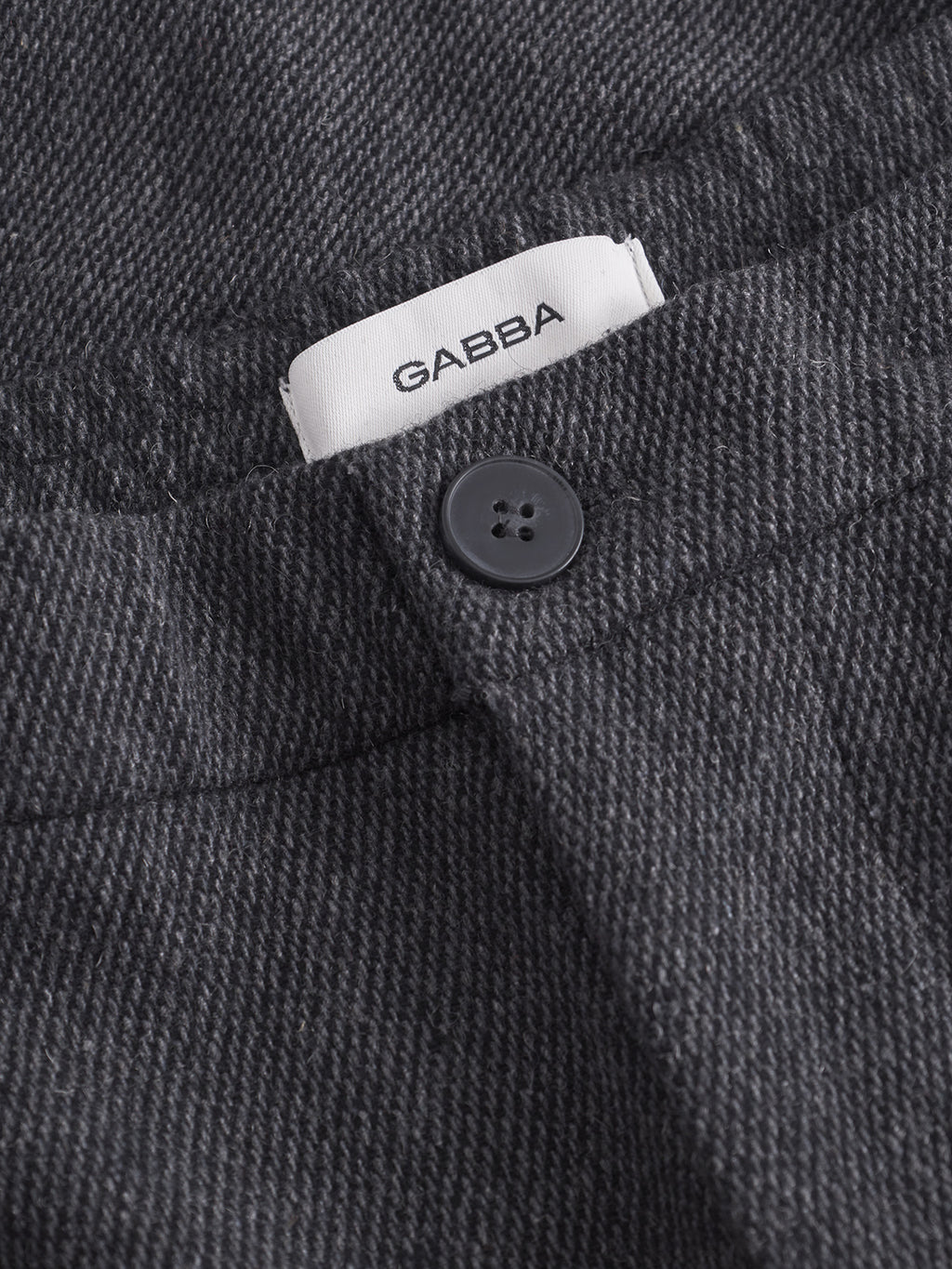 Close-up of Gabba Monza Wook pants in dark grey, featuring a textured fabric, black button, visible white Gabba label, and an elasticated waistband for enhanced comfort.
