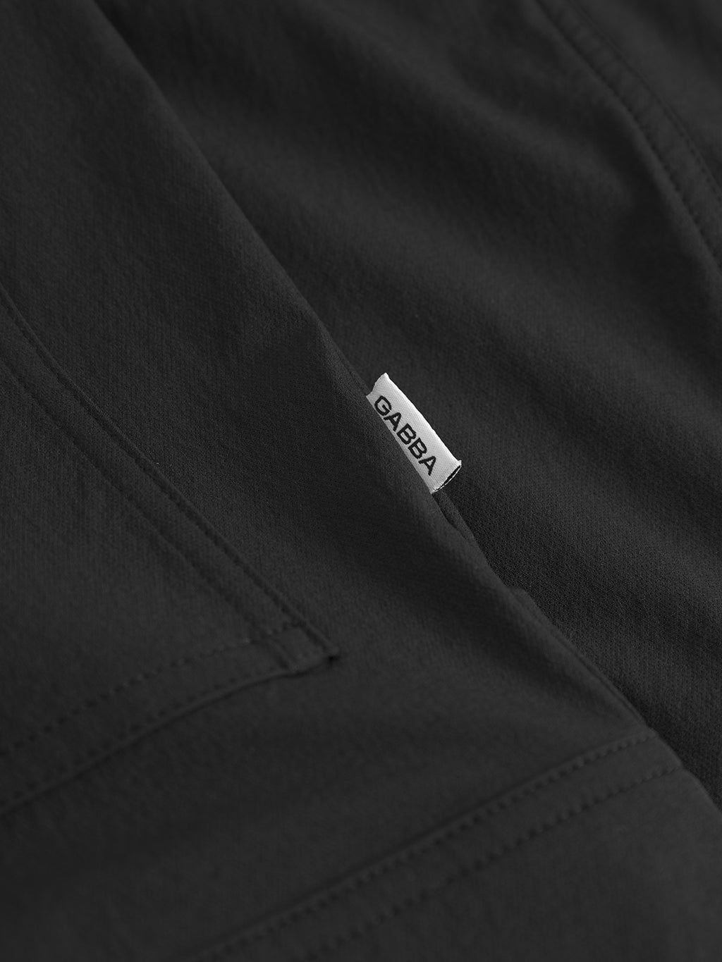 Close-up of the Gabba Koy Tech - Black utility jacket featuring a small white fabric tag with BABA sewn into the seam near a pocket.