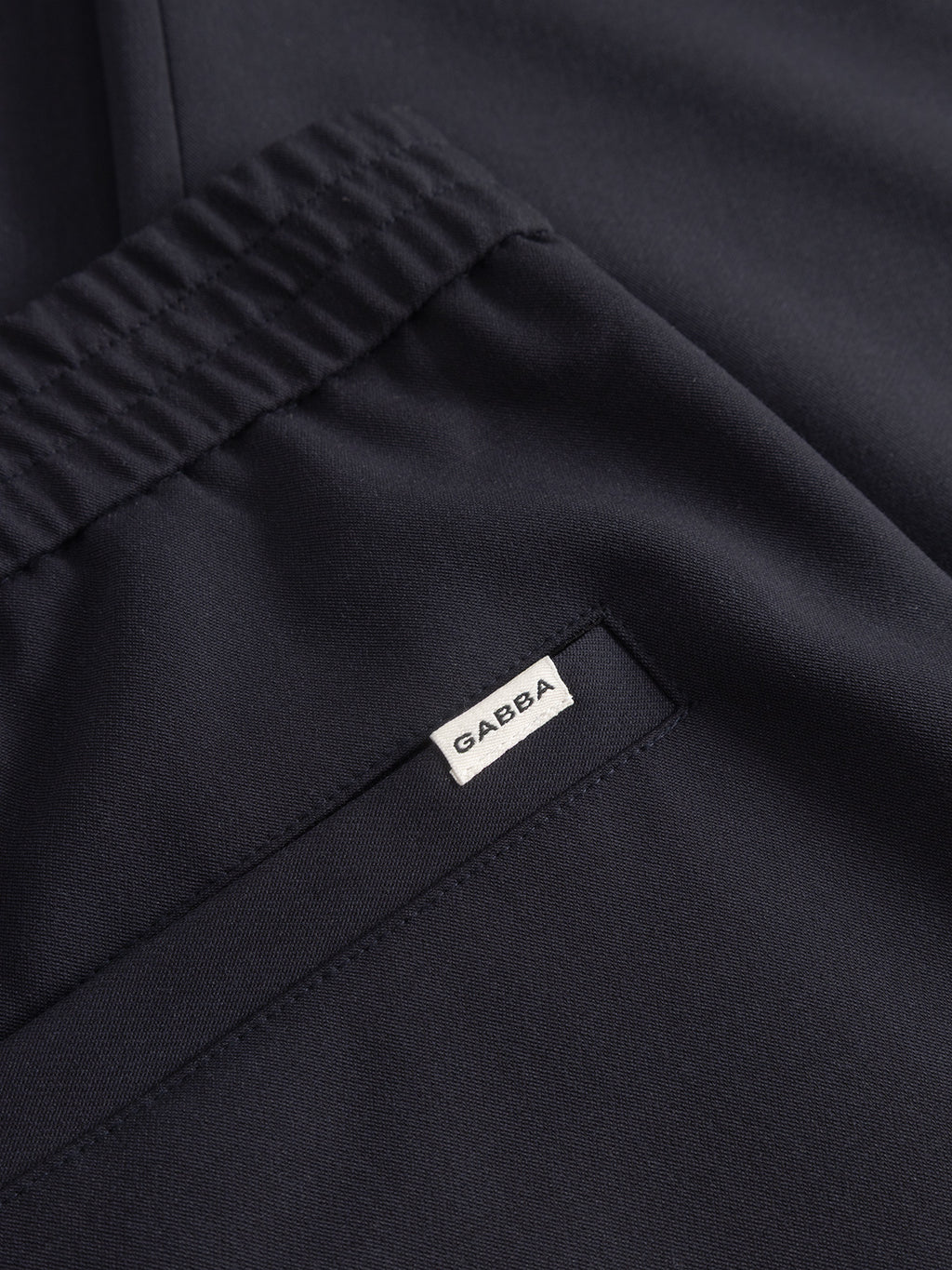 Close-up of Napoli 19 Phin GRS - Navy tailored pants by Gabba, made from recycled wool-blend with elastic waistband, small pocket, and a white GAEBA label—a modern wardrobe staple.
