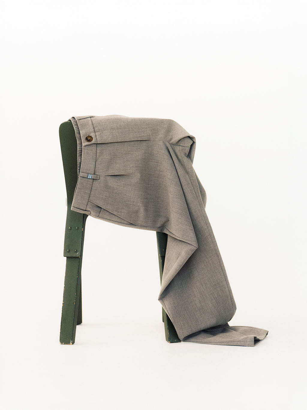 A pair of Gabba GABnapoli 19 Phin GRS - Lt. Grey pants drapes over the backrest of a simple green wooden chair, set against a plain white background.