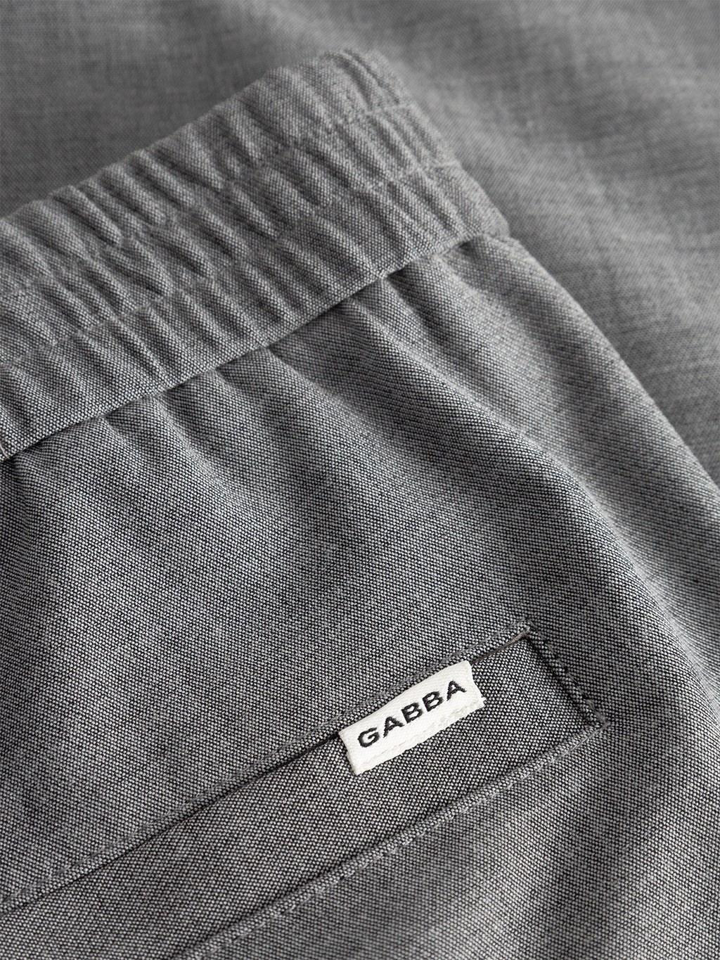 Close-up of Napoli 19 Phin GRS trousers in light grey by Gabba, featuring an elastic waistband and a back pocket with a small white Gabba label—a modern menswear essential.