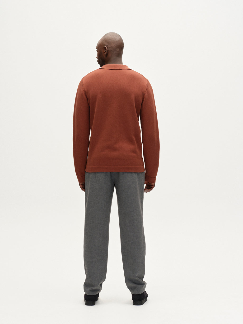 A man stands with his back to the camera, wearing Gabba Napoli 19 Phin GRS trousers in dark grey and a rust long-sleeve shirt, set against a plain white background.