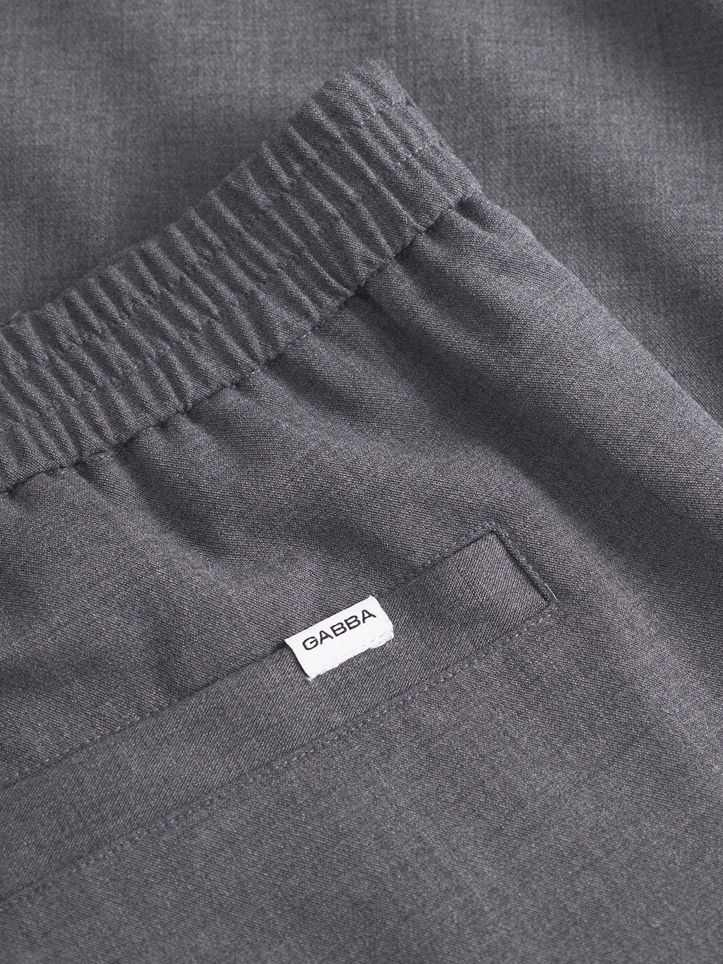 Close-up of Gabba Napoli 19 Phin GRS trousers in dark grey, crafted from a wool-viscose blend with a gathered elastic waistband, back pocket, and a small white GAEBA tag above the pocket.