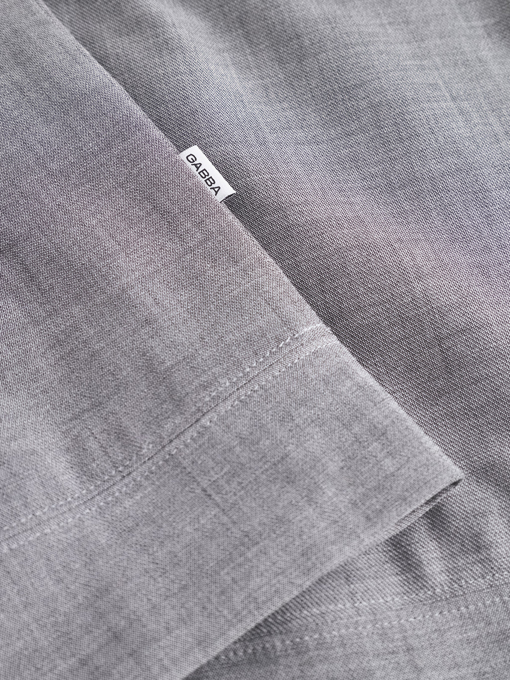 Close-up of light grey GABnik Phin GRS jacket by Gabba, showing finely woven, smooth fabric with a visible seam and a small white CALEBA label attached at the seam, reflecting modern style.