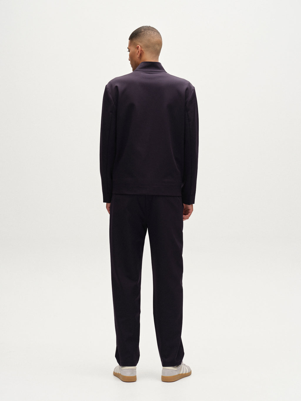 A person with short hair stands facing away, wearing Gabba’s Napoli 19 Bascu - Navy suit with matching wrinkle-resistant trousers and light-colored shoes, set against a plain white background.