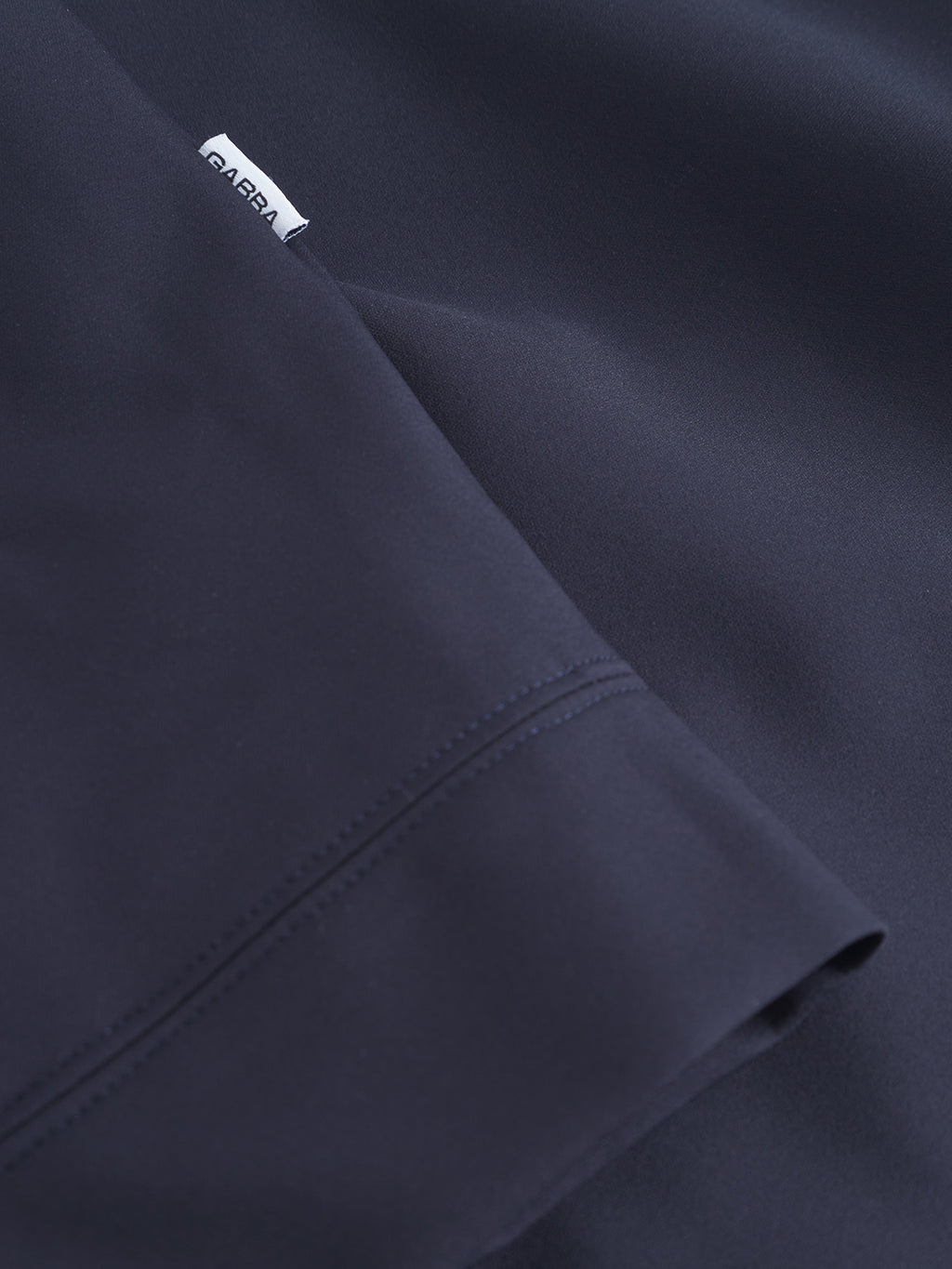 Close-up of dark navy blue fabric from the Gabba Nik Bascu - Navy lightweight jacket, showing a stitched seam and a small white label with the Gabba brand name.