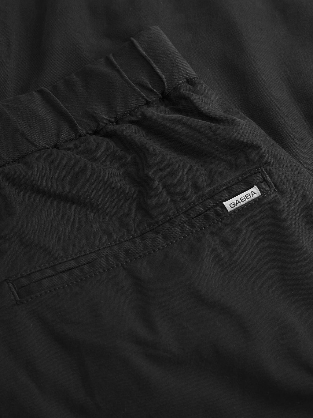 Close-up of the back pocket on Gabba’s Imola Kuadro - Black wide-leg pants, showing a small white fabric label with the brand’s name above the pocket. Smooth, garment-dyed stretch fabric offers comfort and style.