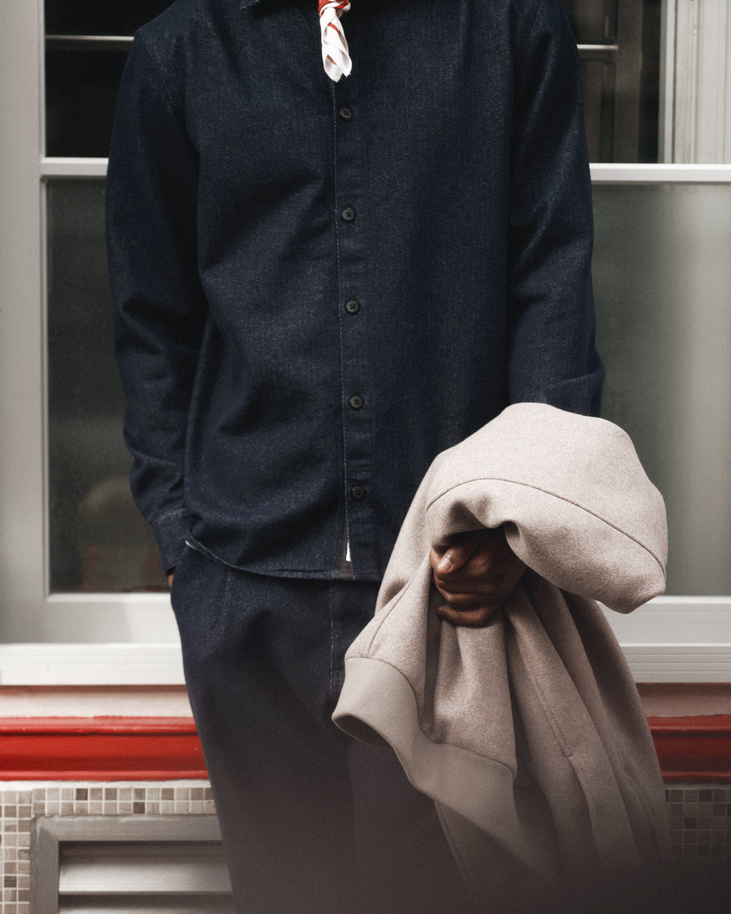 Wearing the Gabba Sven Reg Chev shirt in Dark Navy, a person holds a light-colored coat in their left hand and stands by a window, with their face out of the frame.