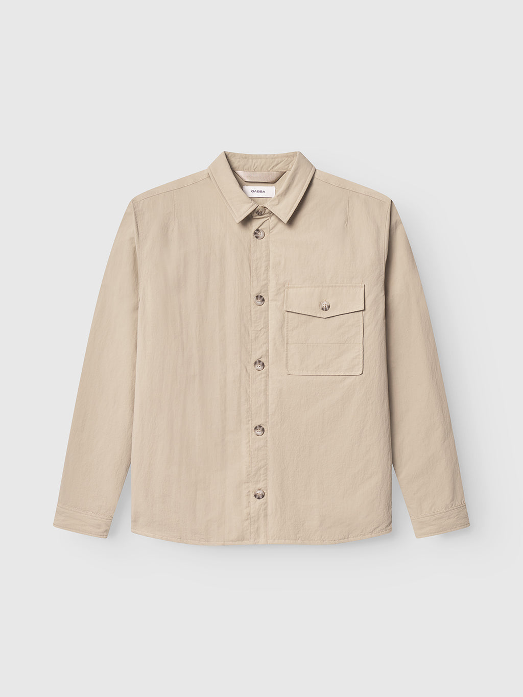 The Gabba Nara Goz - Lt. Sand is a beige, lightly padded regular fit overshirt with long sleeves, a collar, and a single buttoned chest pocket, shown on a white background.