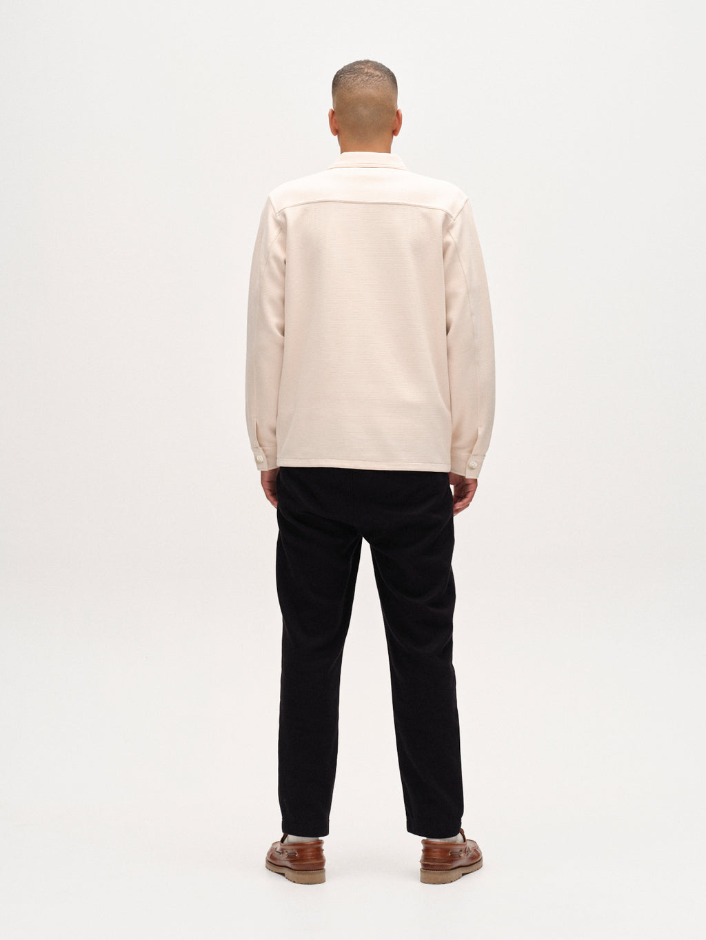 Person wearing a beige shirt and black pants on a white background