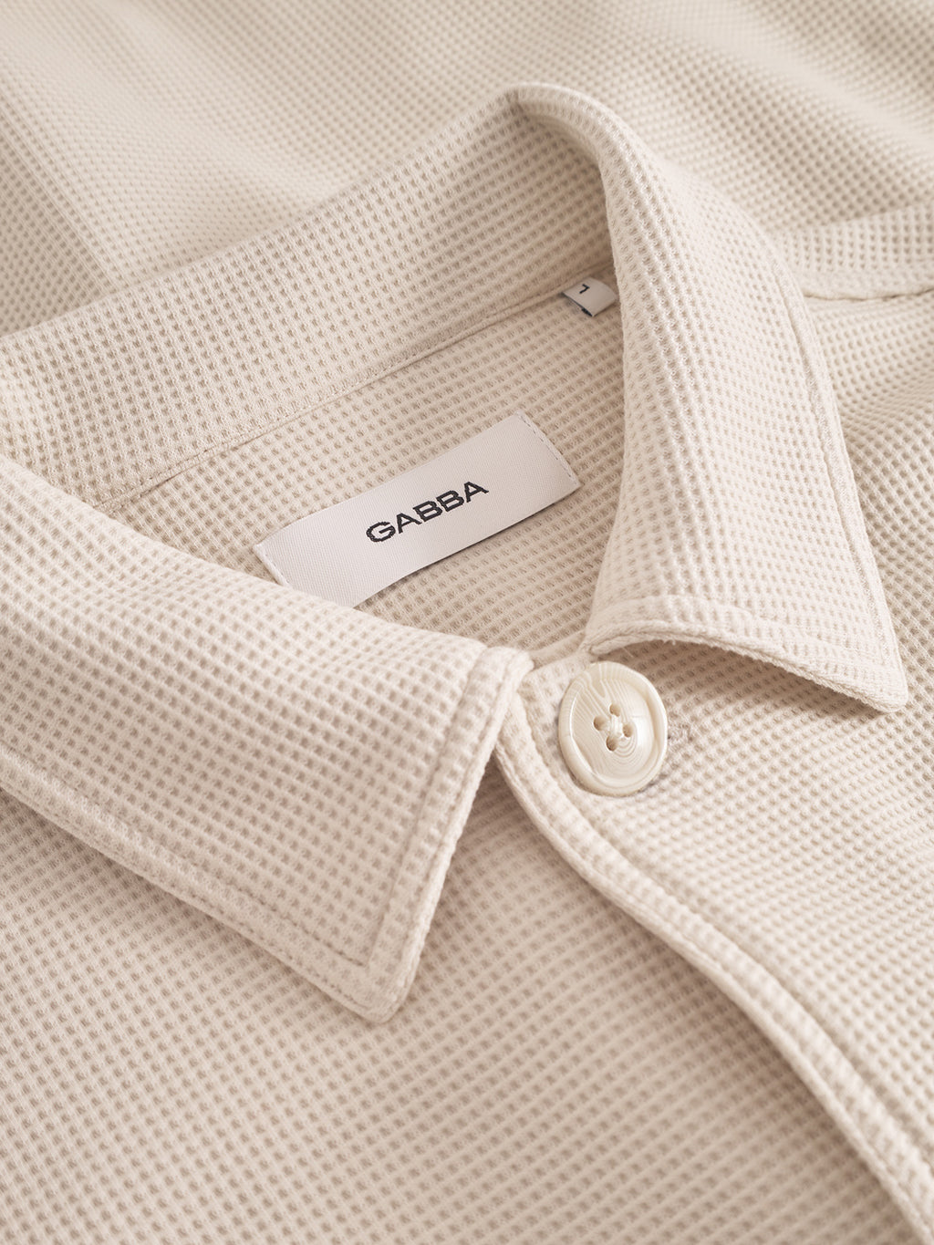 Close-up of a beige textured shirt with a button and 'GABBA' label.