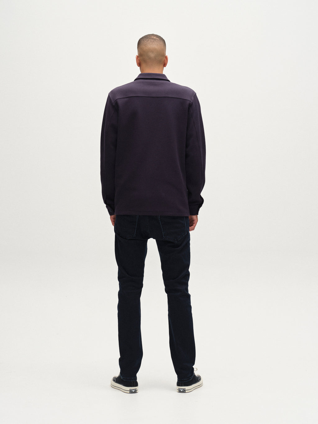 A person stands facing away from the camera against a plain white background, wearing the Gabba Como Waff overshirt in navy, paired with dark jeans and sneakers.