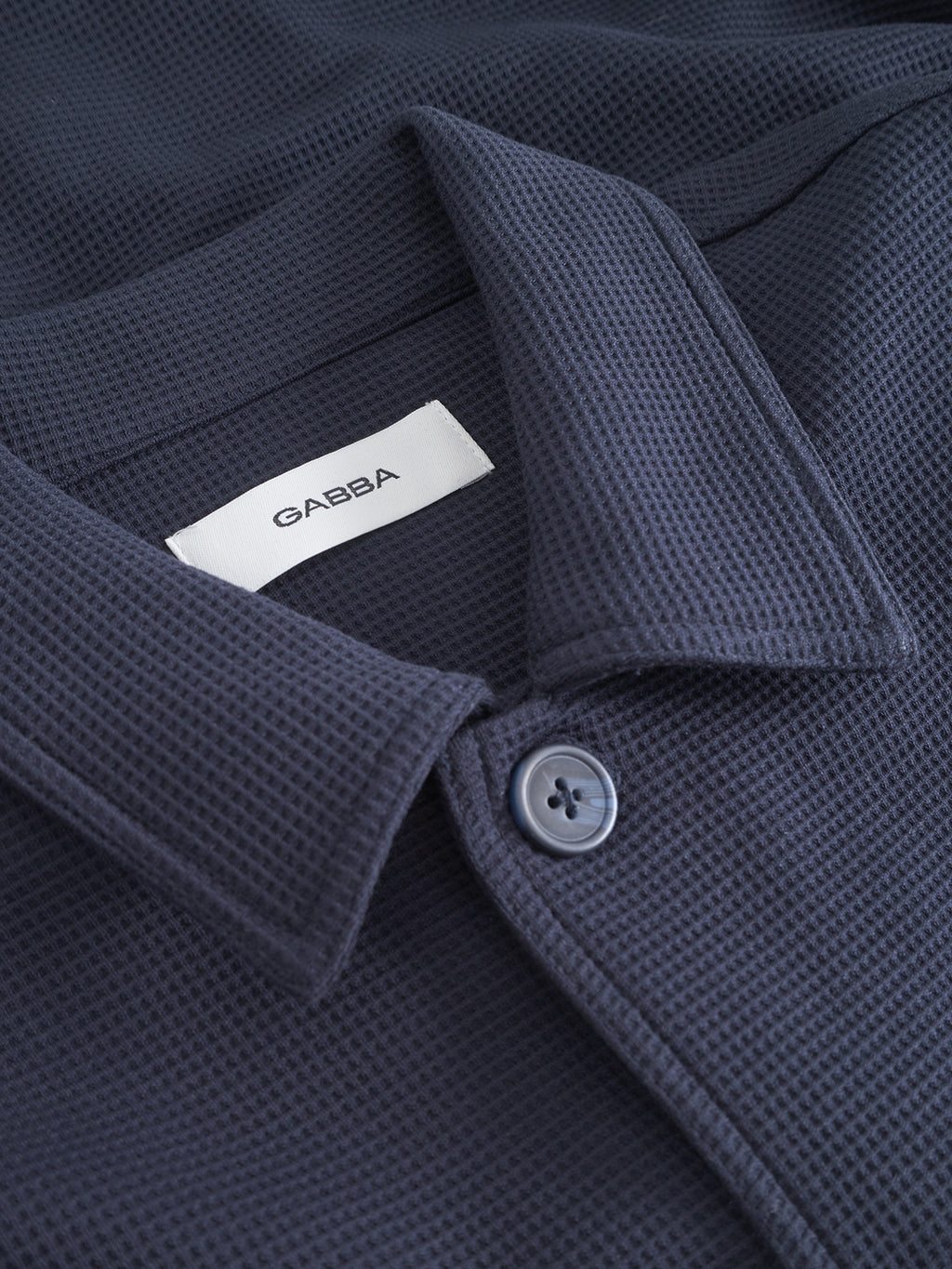 Close-up of the Gabba Como Waff - Navy overshirt, featuring a subtle waffle-knit grid texture, button-up collar, and a visible “Gabba” label for a stylish finish.