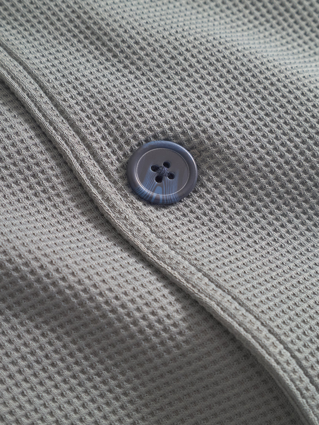 Close-up of Gabba’s Como Waff overshirt in Dust Sage Green, featuring textured waffle-knit fabric and a black plastic button by the seam. The distinctive weave adds depth, making it ideal for layering on cooler days.
