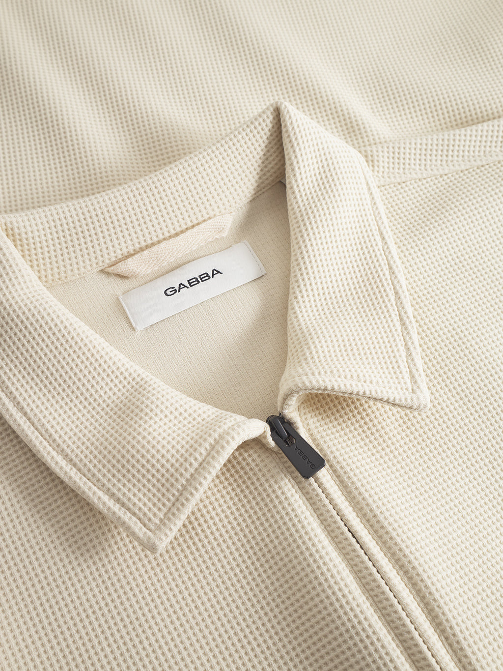 Close-up of the Gabba Island Waff - White Almond shirt, featuring a beige waffle knit texture, pointed collar, and an inner Gabba label. Its unique weave makes this hybrid shirt a standout piece in mens fashion.
