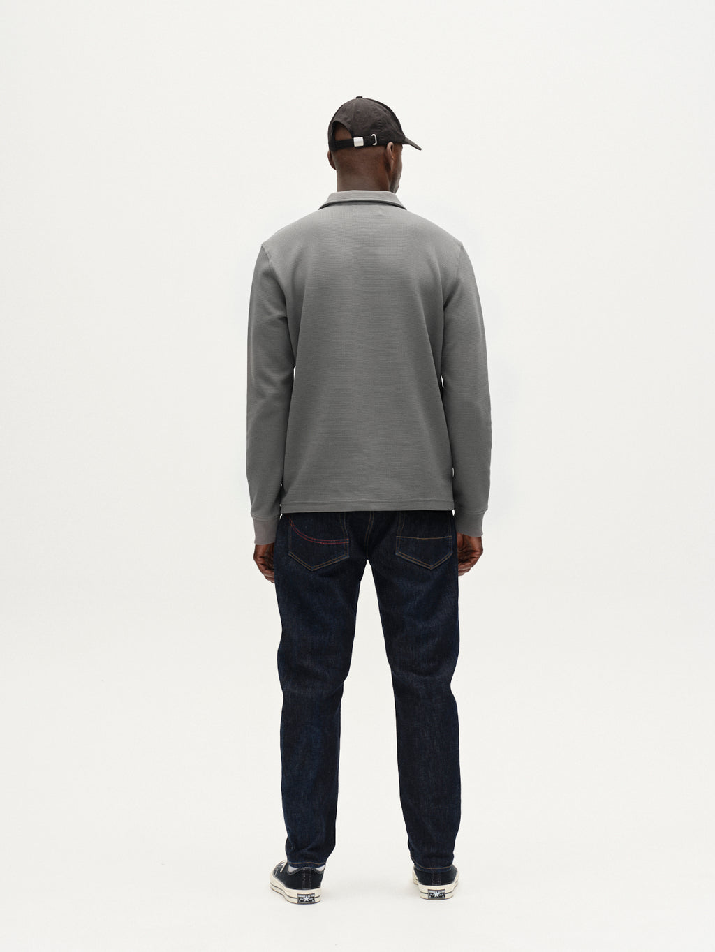 A person wearing the Gabba Island Waff - Dust Sage Green textured long-sleeve shirt, a black cap, and dark jeans stands with their back to a plain white background.
