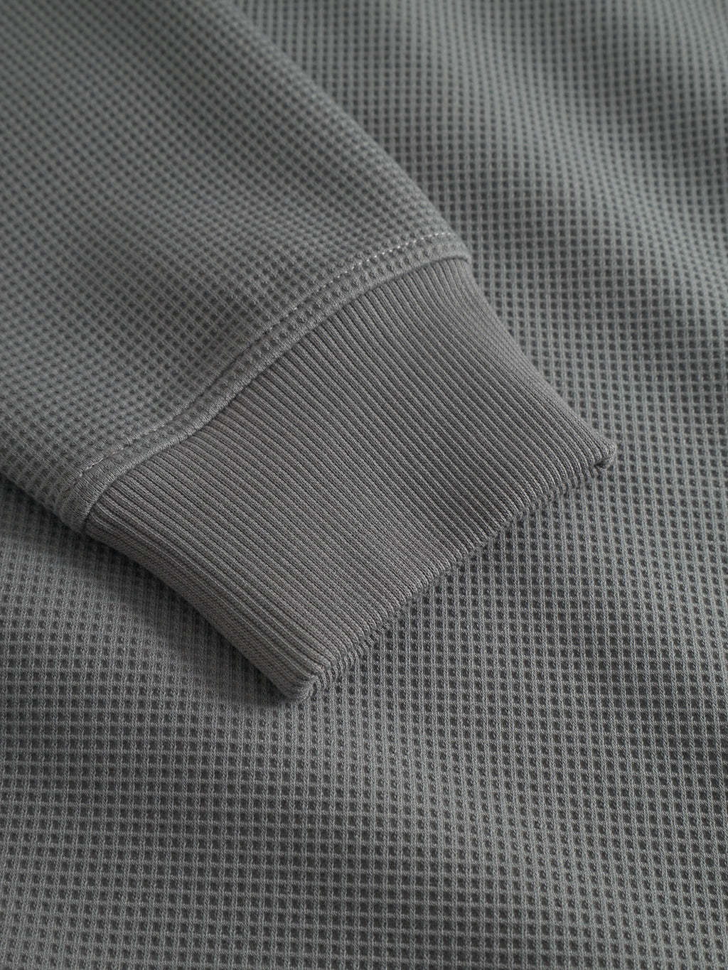 Close-up of the Gabba Island Waff long-sleeve shirt in Dust Sage Green, featuring a textured waffle surface and ribbed wrist cuff.