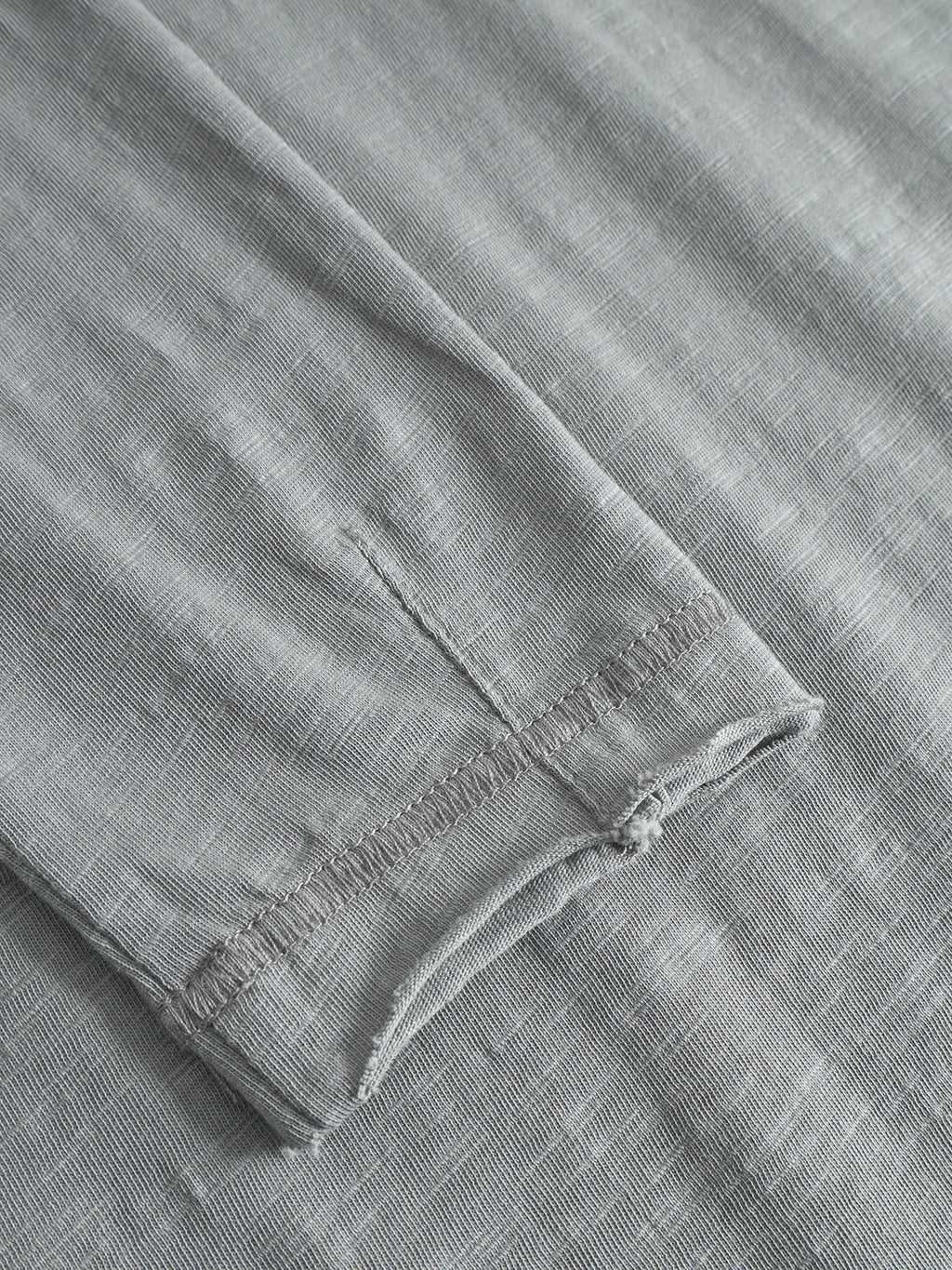 Close-up of a Gabba Kostant New LS long-sleeved t-shirt in Dust Sage Green, highlighting the textured slub jersey fabric, visible stitching, and seam detail as it lies flat on a matching background.