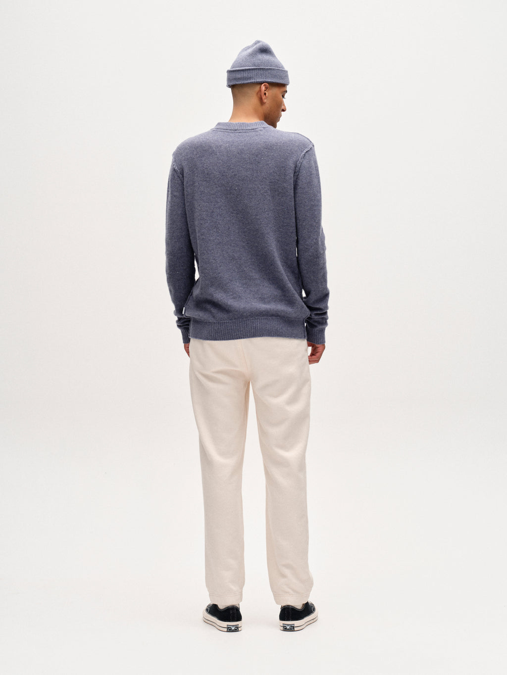A person stands facing away against a plain white background, wearing Gabbas Joe-Pas Vill relaxed-fit cotton twill trousers in Lt. Sand, paired with a gray beanie, gray long-sleeve sweater, and black shoes.