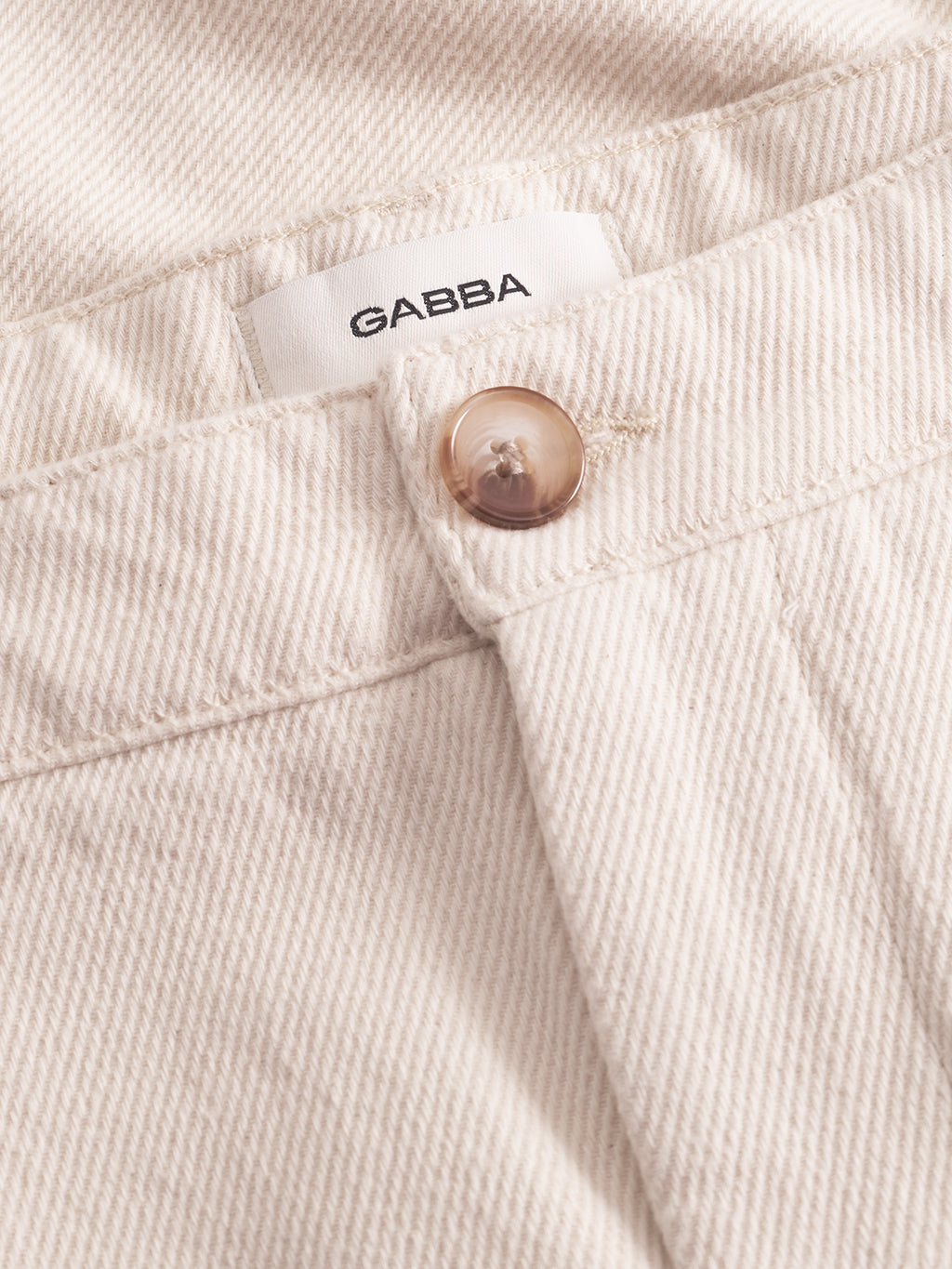Close-up of Gabba Joe-Pas Vill - Lt. Sand beige cotton twill pants featuring a brown button, front belt loop, and a white Gabba label sewn inside the waistband—an everyday essential.
