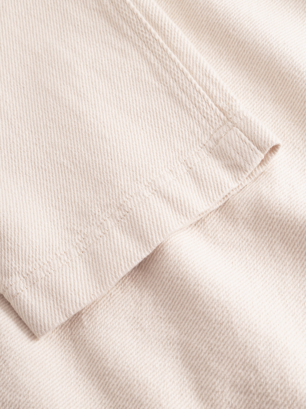 Close-up of Gabba Joe-Pas Vill - Lt. Sand: beige cotton twill with visible diagonal weave and hem stitching, highlighting a wardrobe essential like relaxed-fit trousers or a jacket.