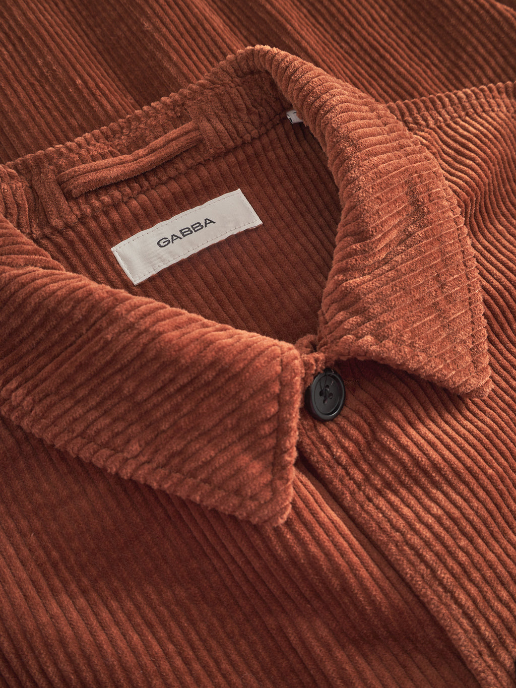 Close-up of the Gabba Libre AX Cord overshirt in brown rust, showcasing its visible collar, black button, and inner white Gabba label.