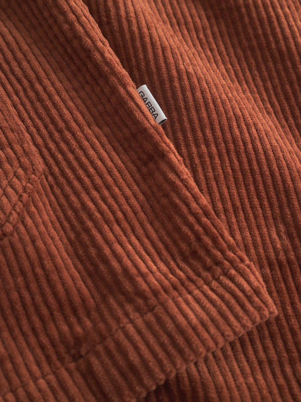 Close-up of the Gabba Libre AX Cord overshirt in brown rust, featuring soft corduroy ridges and a small white ABBA tag on the seam—ideal for men seeking a textured, easy-to-layer shirt style.