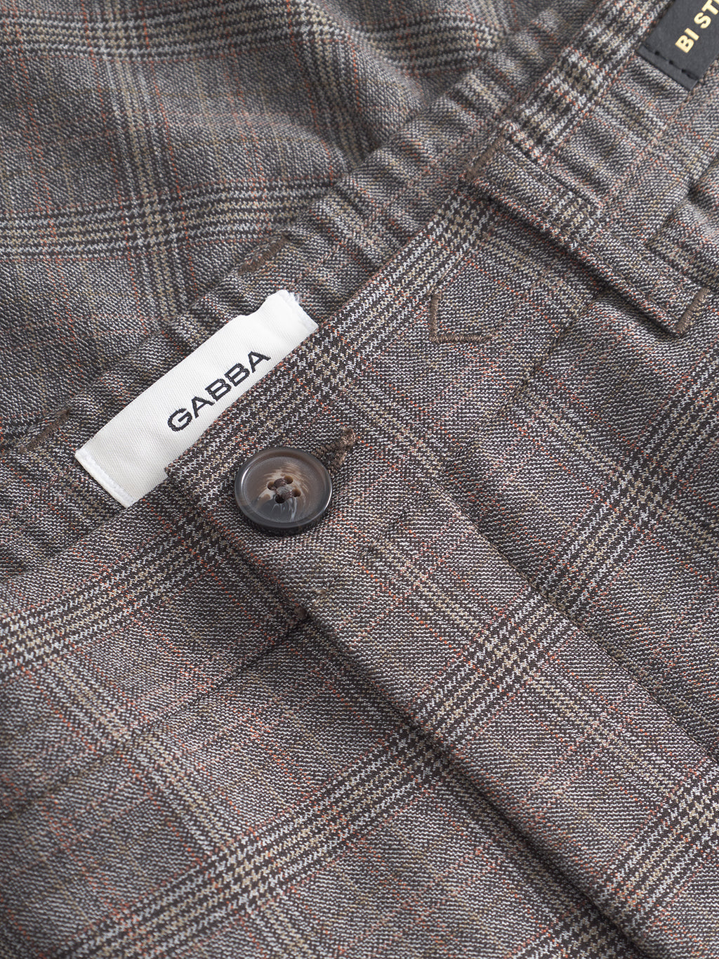 Close-up of Gabba Monza Tinun - Brown Check trousers in a regular straight fit, featuring bi-stretch comfort fabric and a brown check pattern with thin red lines. A visible white label reads GAEBA above the button.