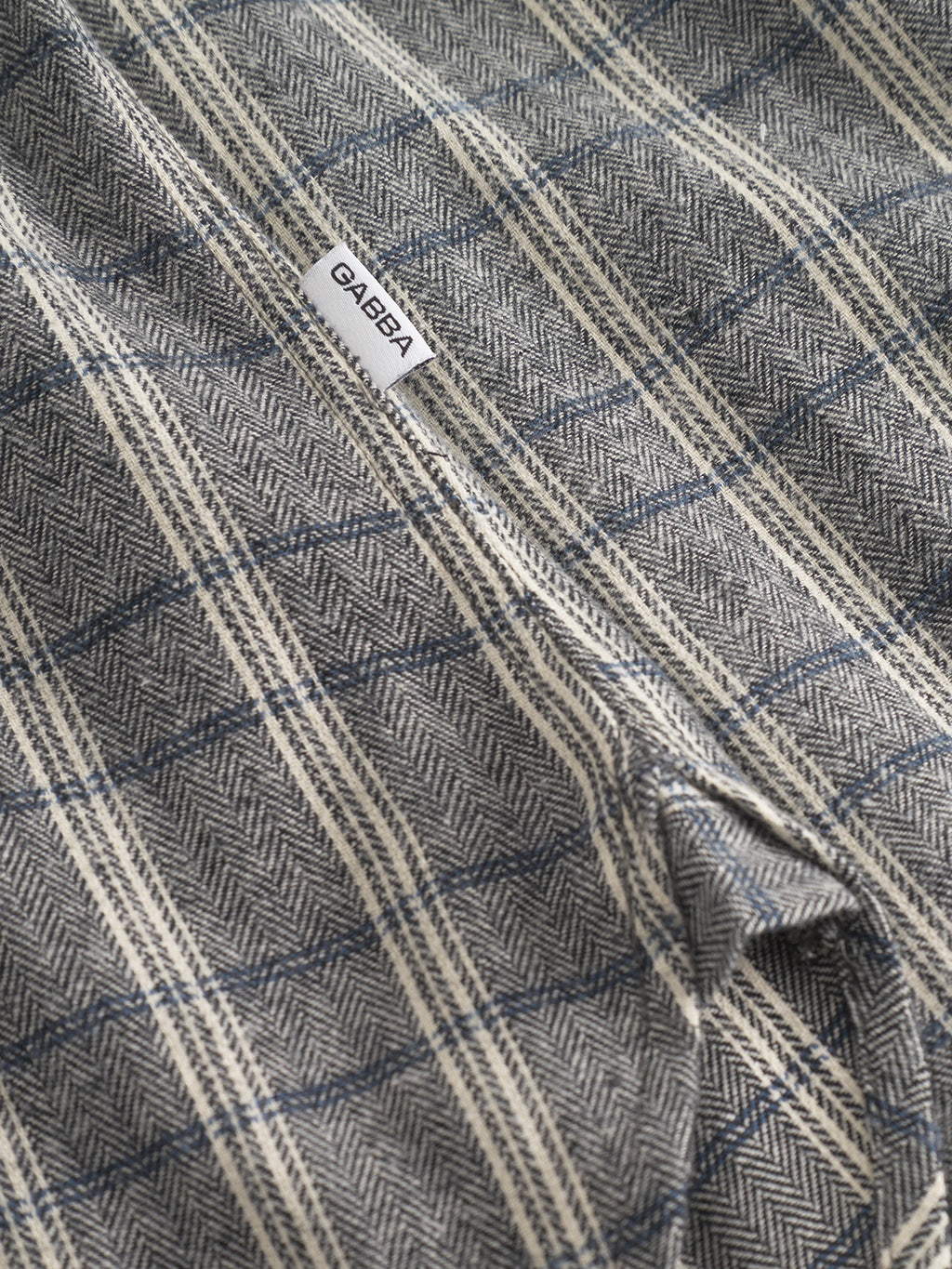 Close-up of Gabbas Sven Reg Herri LS - Grey shirt, featuring gray and cream plaid herringbone fabric and a sewn-in white label.