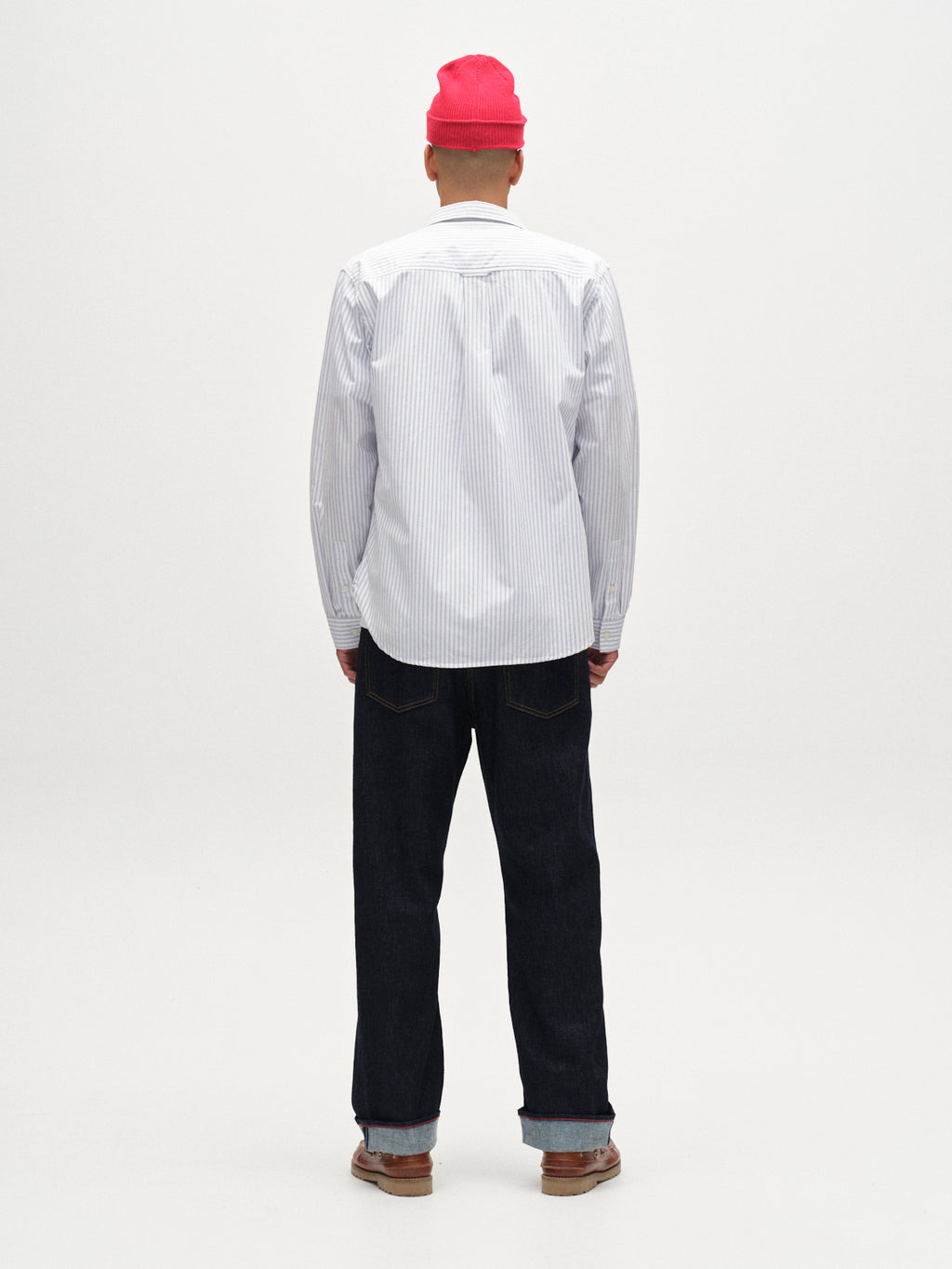 A person faces away from the camera wearing a pink beanie, dark jeans, brown shoes, and the Gabba Sven Reg Clo Ls - White Stripe 100% cotton shirt, set against a plain white background.
