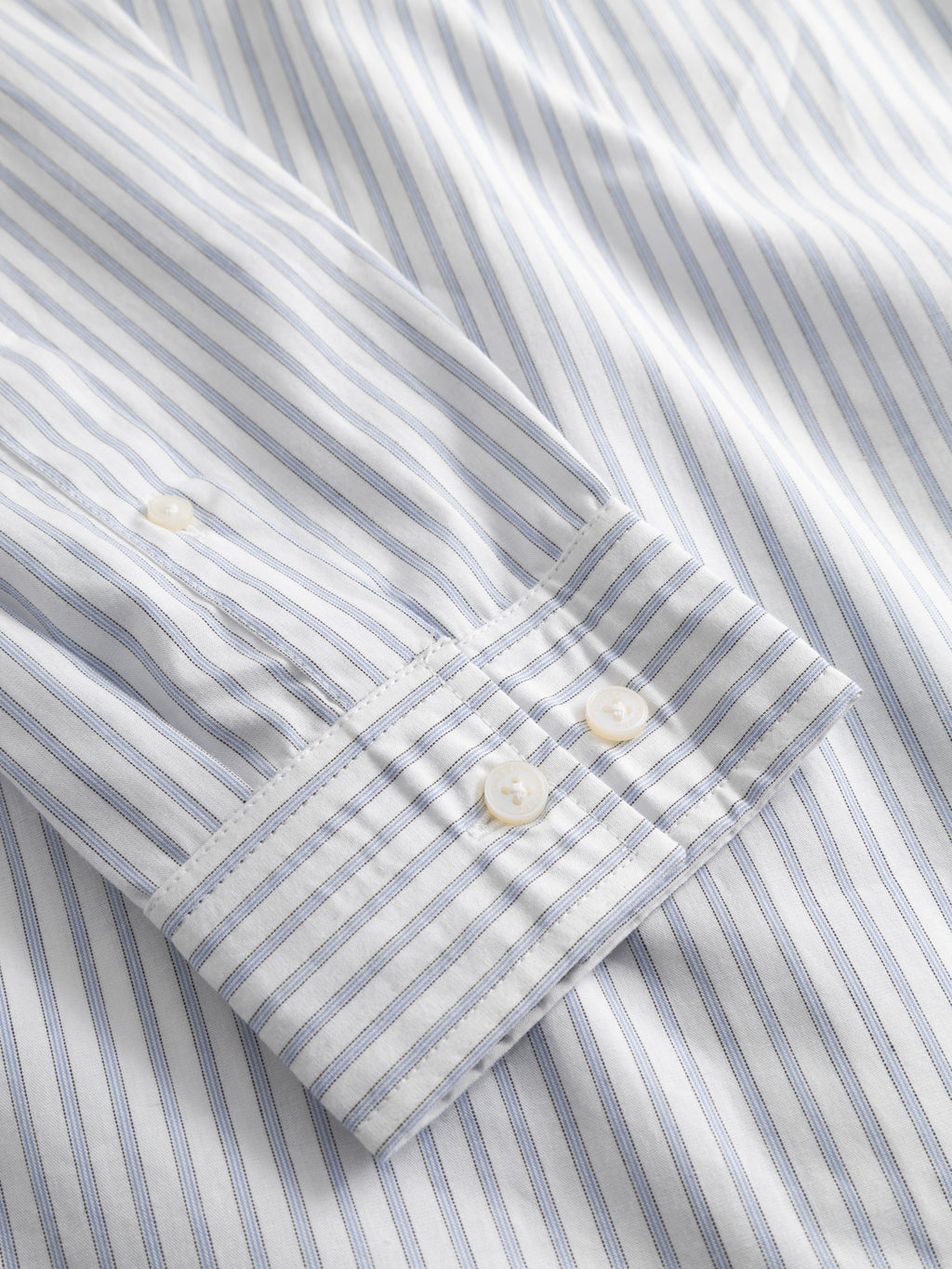 A close-up of the Gabba Sven Reg Clo Ls - White Stripe, a regular-fit 100% cotton shirt featuring thin blue vertical stripes, white cuffs with two buttons, and fine stitching details.