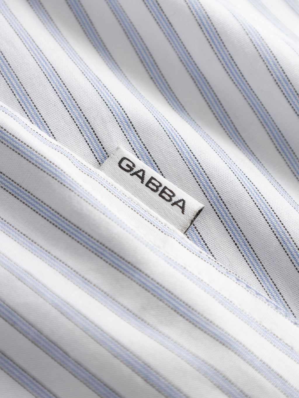 Close-up of the Gabba Sven Reg Clo Ls shirt in white with light blue and gray stripes, made from 100% cotton and featuring a sewn-in GABBA label.