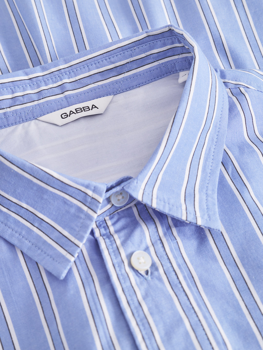 A close-up of the Sven Reg Clo Ls, a light blue and white striped shirt by Gabba, featuring a classic collar and white buttons. Made from 100% cotton.