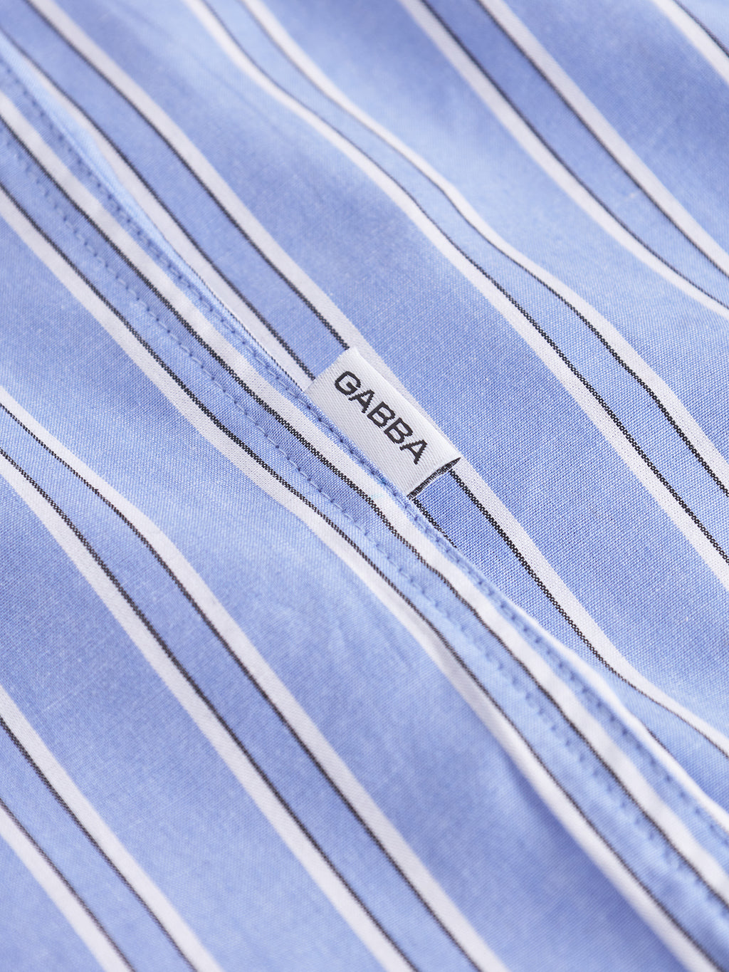 Close-up of the Gabba Sven Reg Clo Ls - Blue Stripe shirt, made from 100% cotton with light blue fabric and vertical white and navy stripes, featuring a small white 