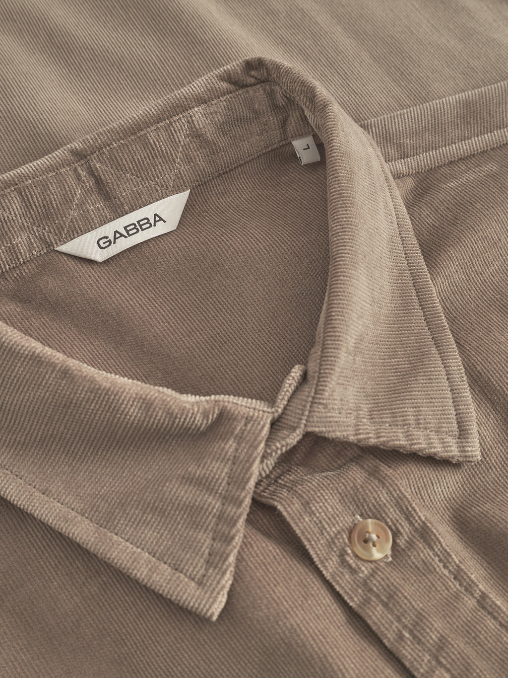 Close-up of the Gabba Jens Over Cord LS in Sand Greige, featuring a folded collar, button detail, and inner white Gabba label. Its corduroy texture and fine stitching make this autumn shirt ideal for layering.