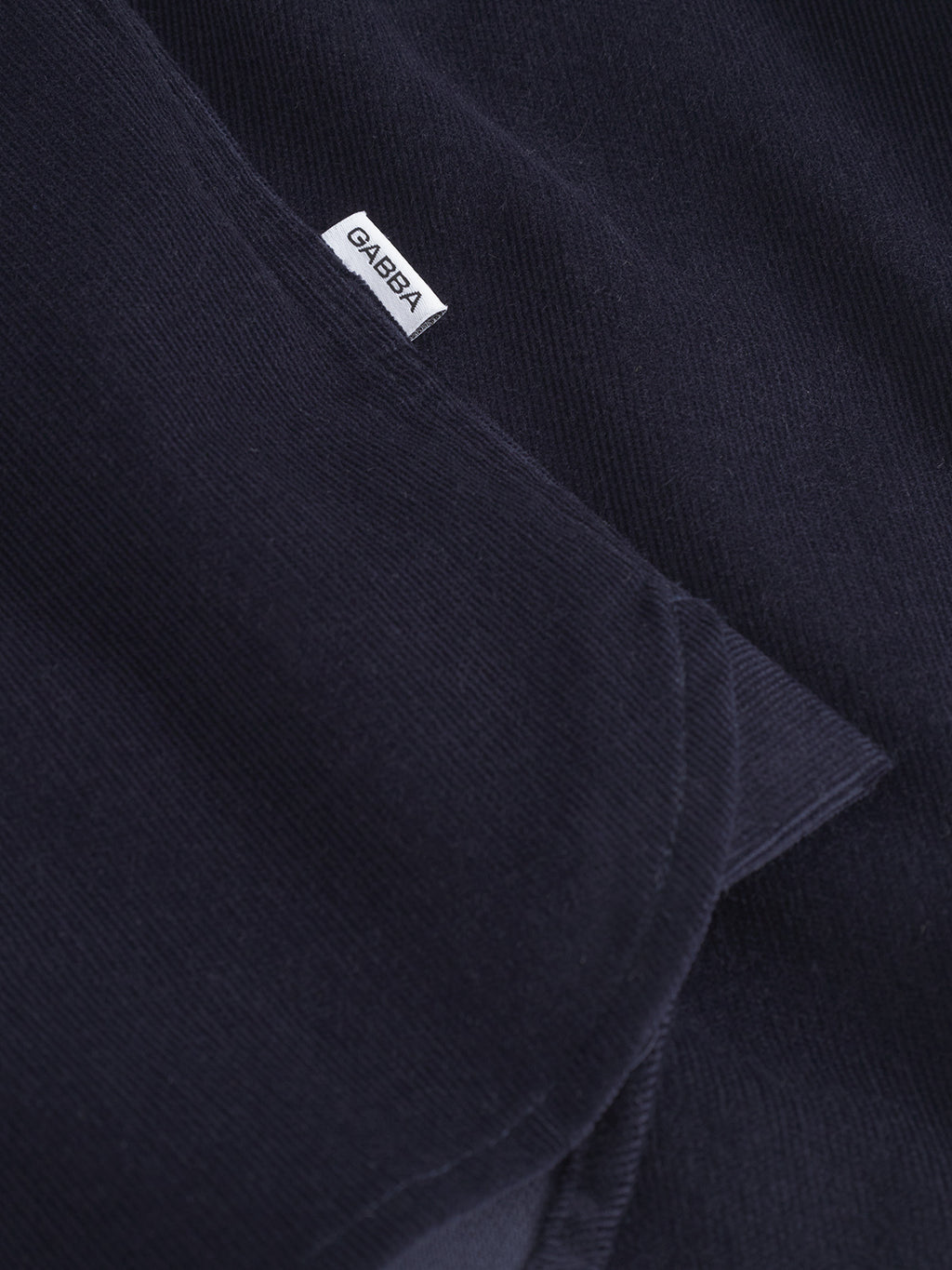 Close-up of the Gabba Jens Over Cord LS - Night Sky, a navy blue corduroy overshirt featuring a white Gabba label. Its rich texture and fine stitching make it an ideal layering piece for any outfit.