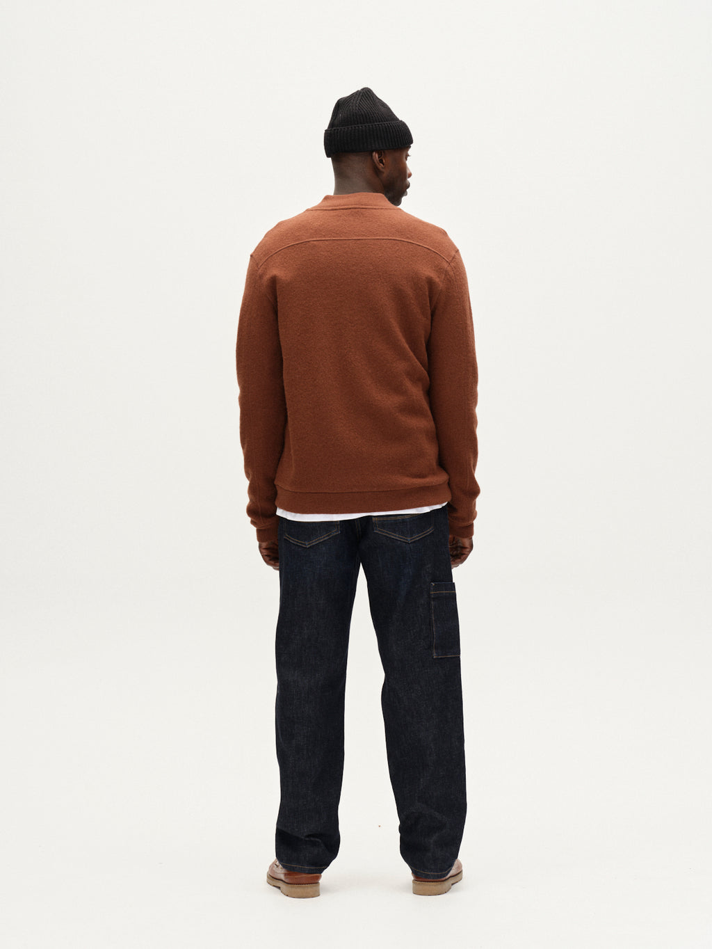 A man faces away from the camera against a plain white background, wearing Gabbas Max Work Self - Dark Blue Denim jeans, paired with a brown jacket, white shirt, brown shoes, and a black beanie for a classic workwear look.