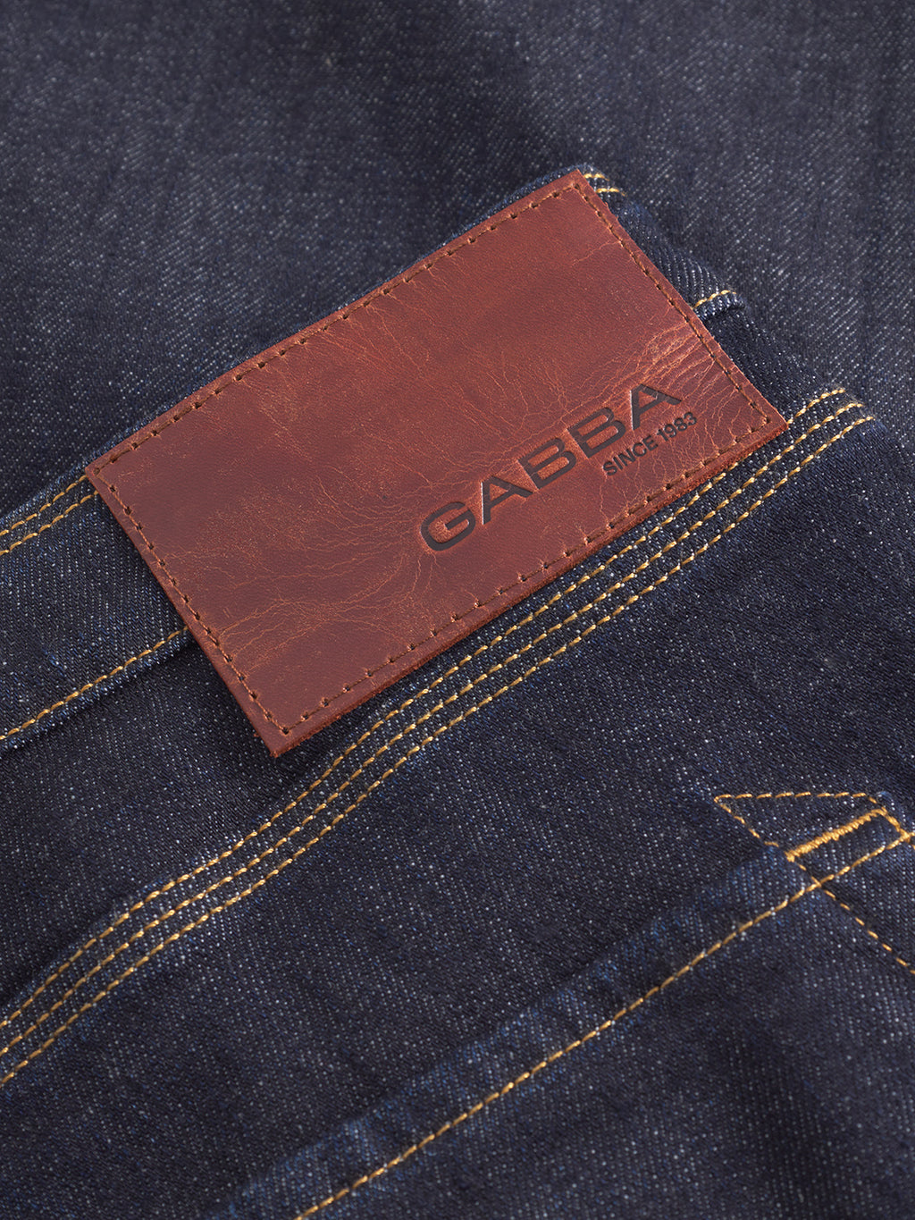 Close-up of Gabbas Max Work Self loose-fit jeans in dark blue denim with yellow stitching, featuring a brown leather patch on the back pocket embossed with Gabba and Since 1983—classic workwear-inspired style.