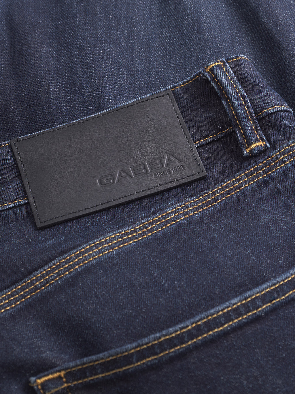 Close-up of Gabba Carl Willo - Mid Blue Denim jeans, featuring a black leather patch embossed with GABBA SINCE 1983, yellow stitching, and a back waistband belt loop in a Japanese-inspired wash.