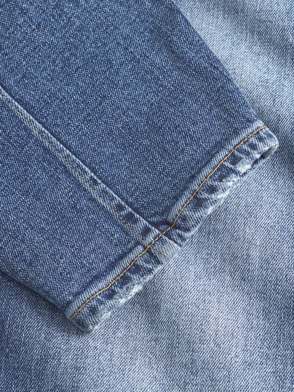 Close-up of the frayed hem on Gabbas Alex Cros - Mid Blue Denim relaxed tapered jeans in comfort stretch fabric, laid over another blue denim piece.